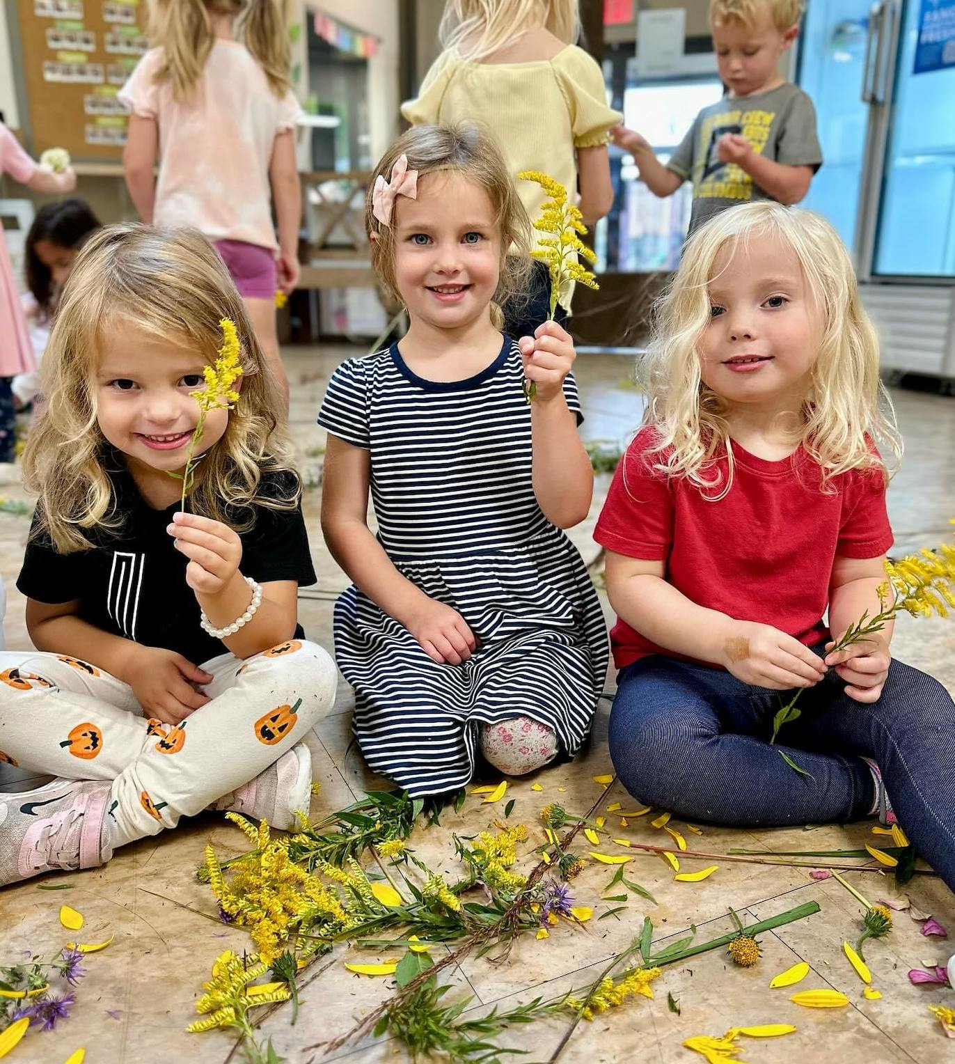 Three children sitting on the floor with flowers