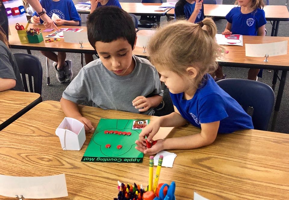 Two children playing with red counters on a green mat at a table