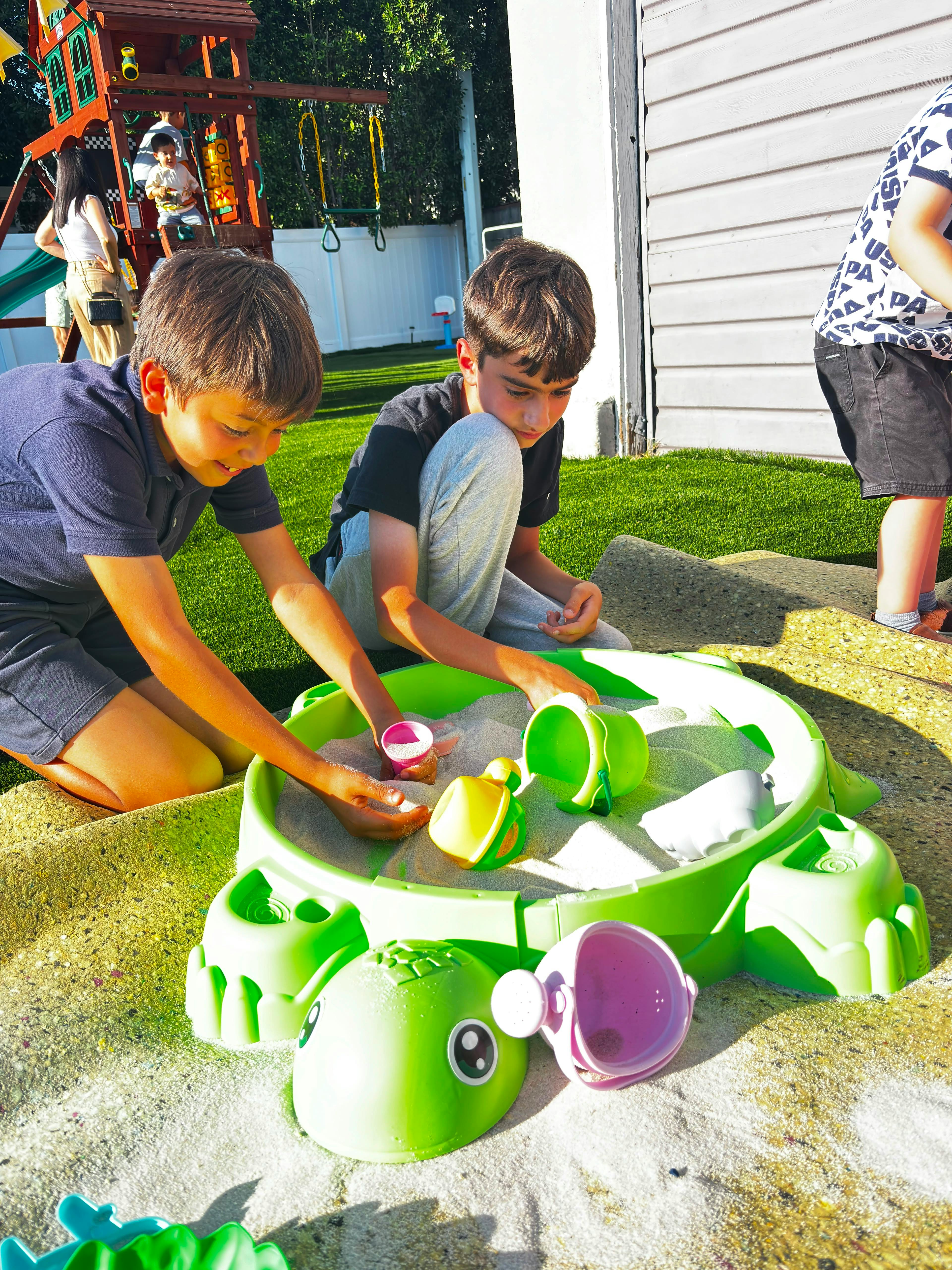 Two children playing in a turtle-shaped sandbox with toy shovels and buckets