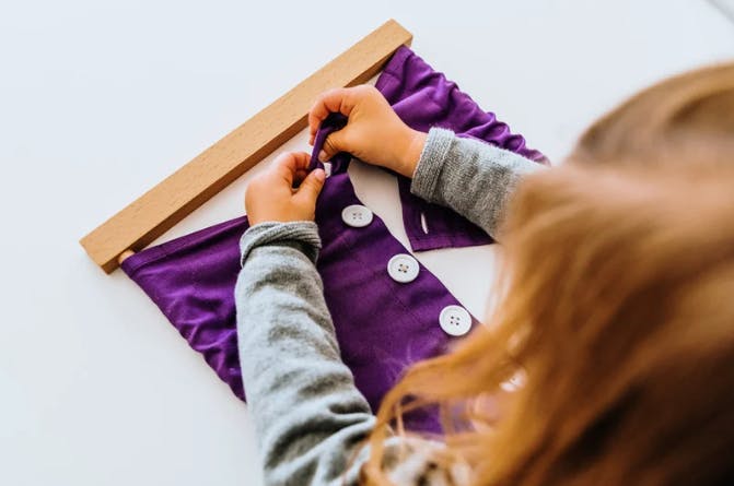 Child's hands working with a purple button frame