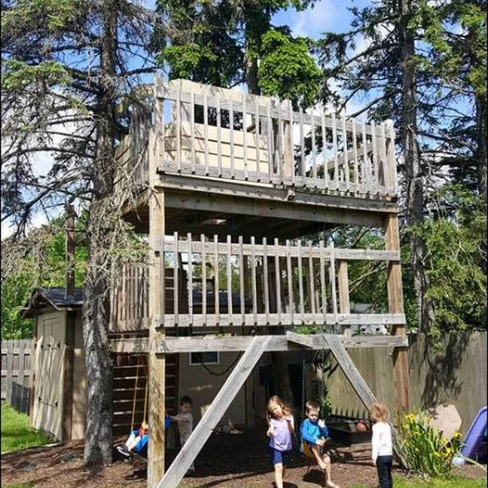 Children playing around a multi-level wooden treehouse structure