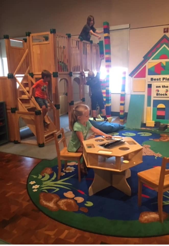 Children playing on a wooden structure and at a table in a play area