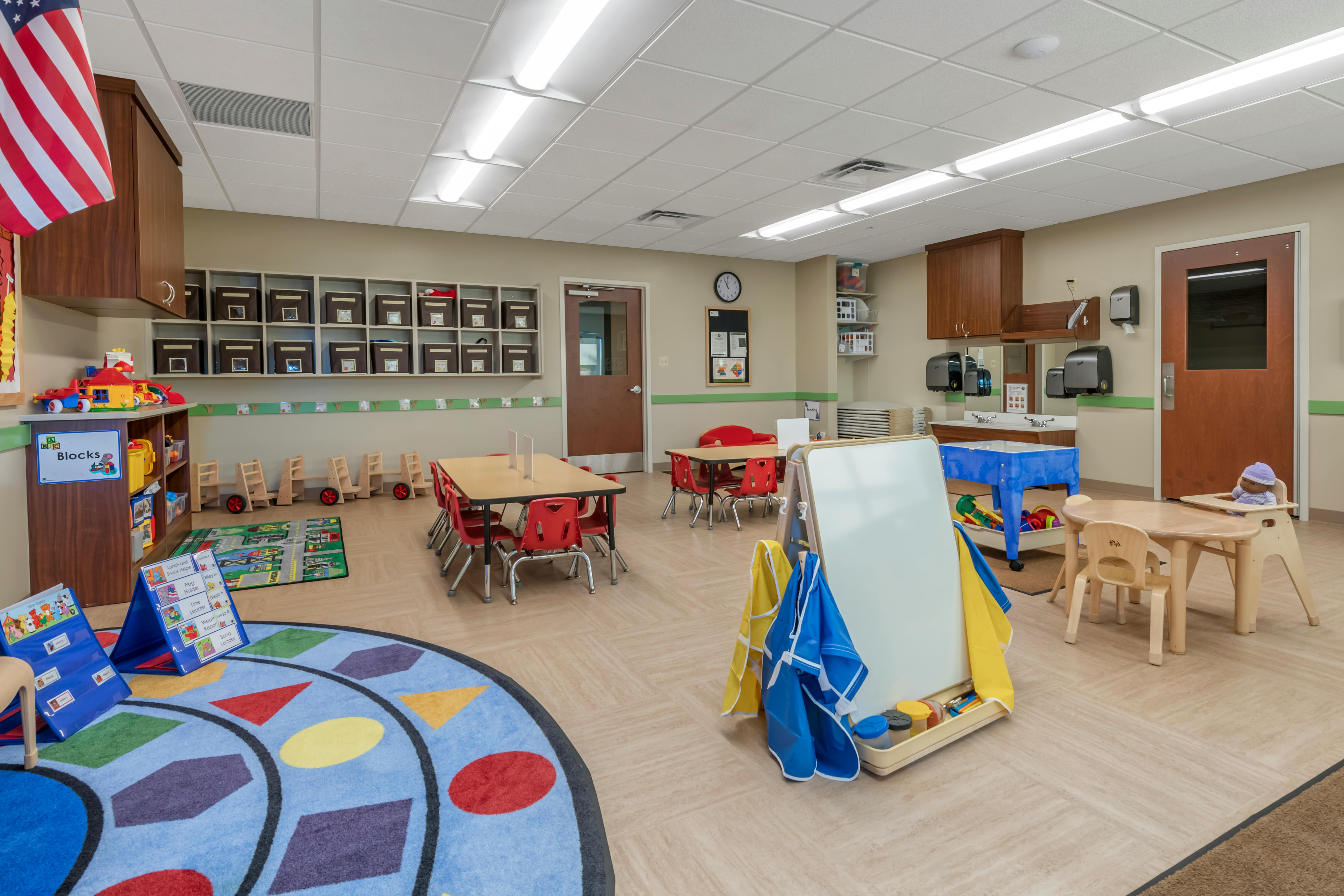Classroom with small tables and chairs, toys, and a colorful rug