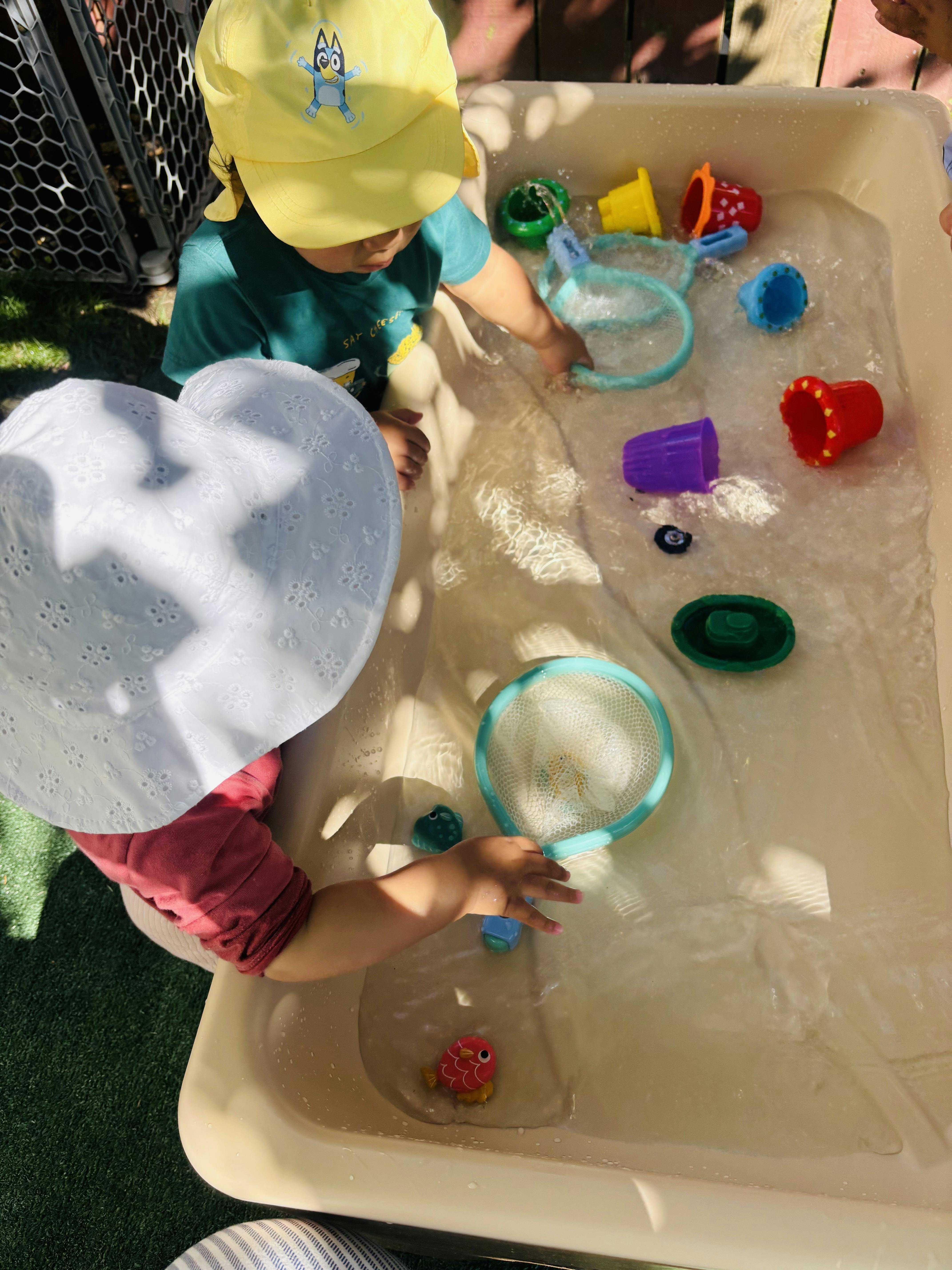 Two children playing with water toys in a water table