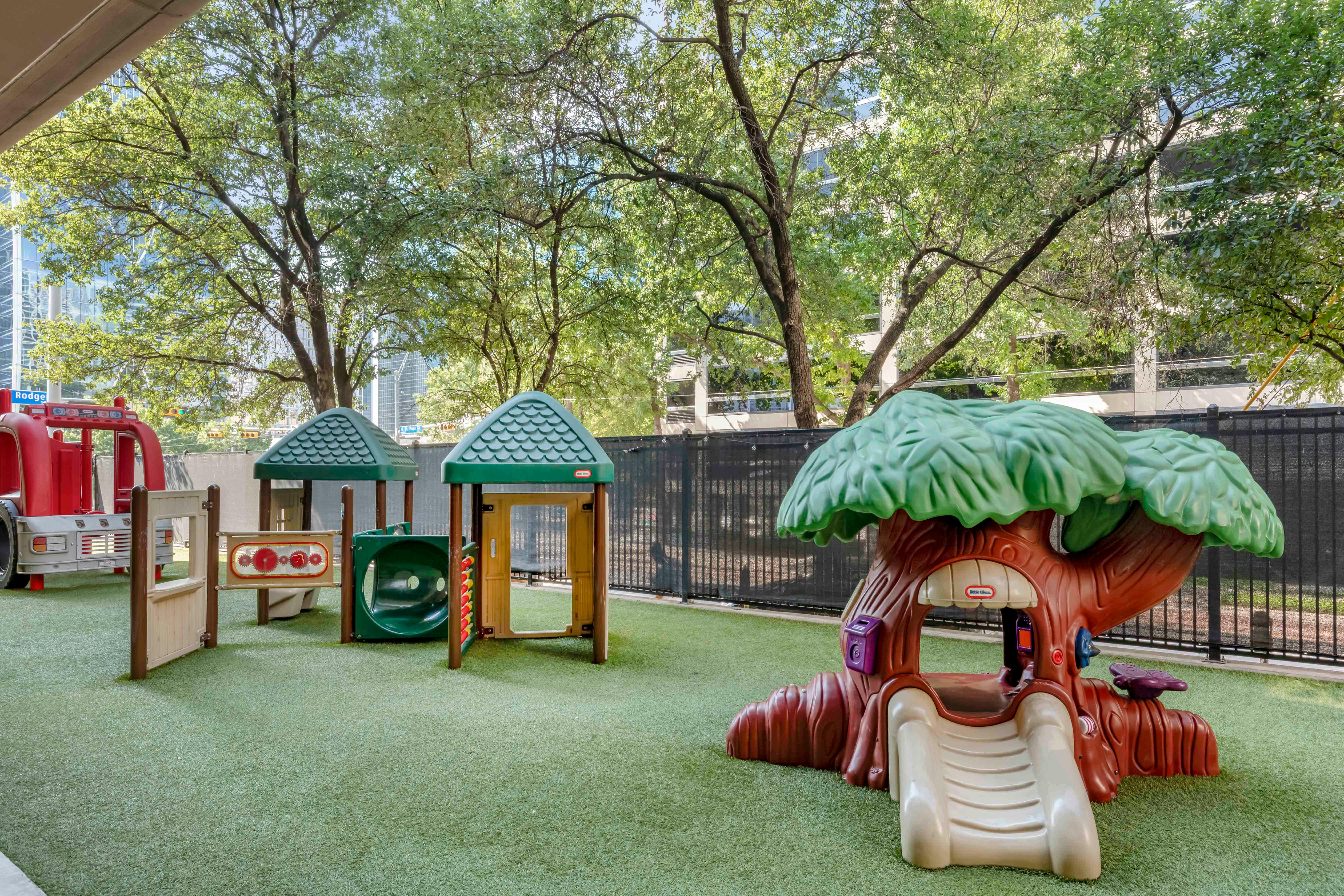 Playground with fire truck, green playhouses, and treehouse slide on artificial turf