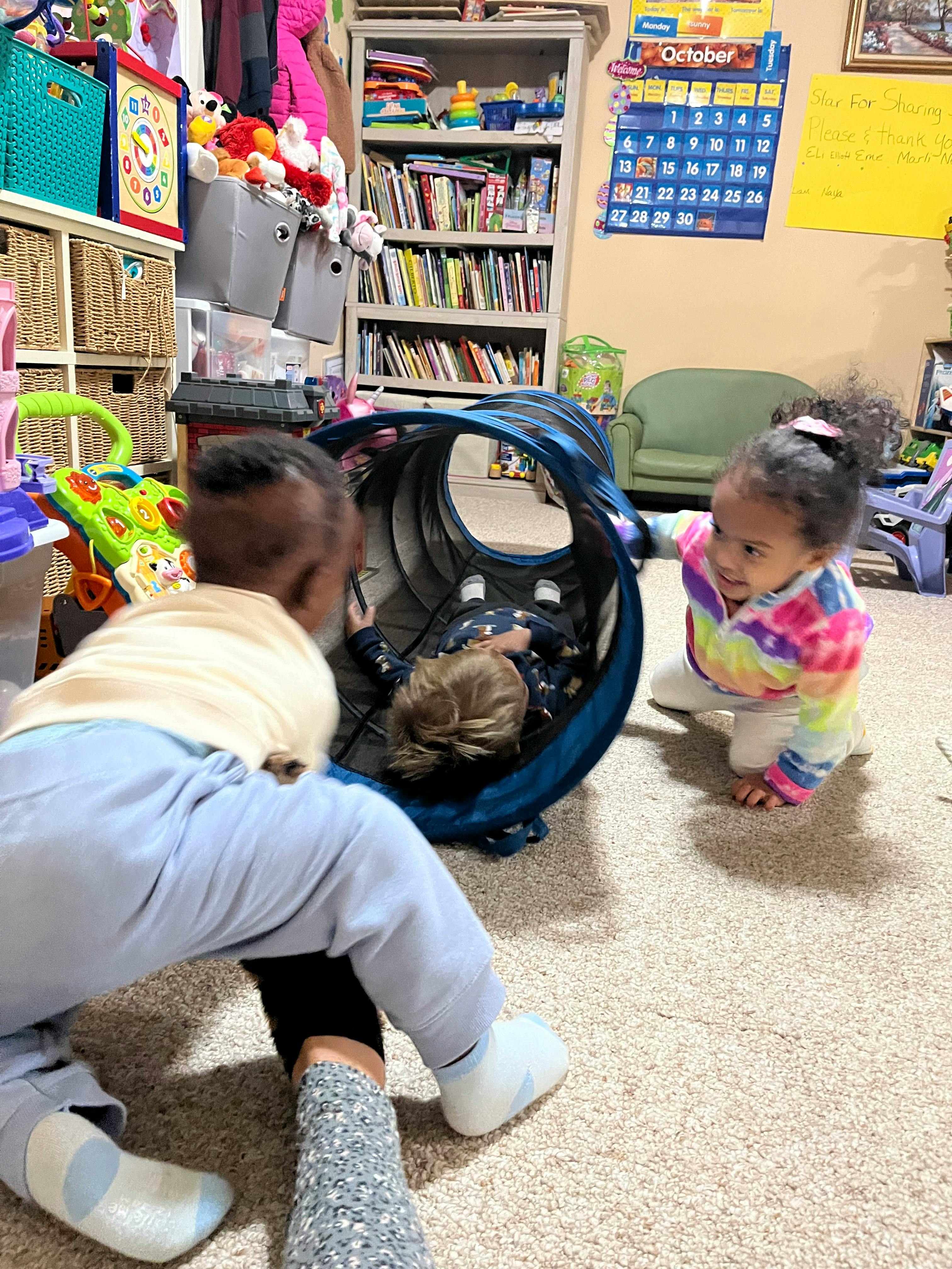 Three children playing with a blue tunnel on a carpeted floor