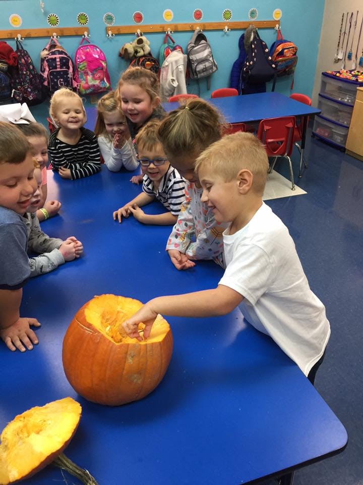 Children gathered around a table, one child reaching into a pumpkin