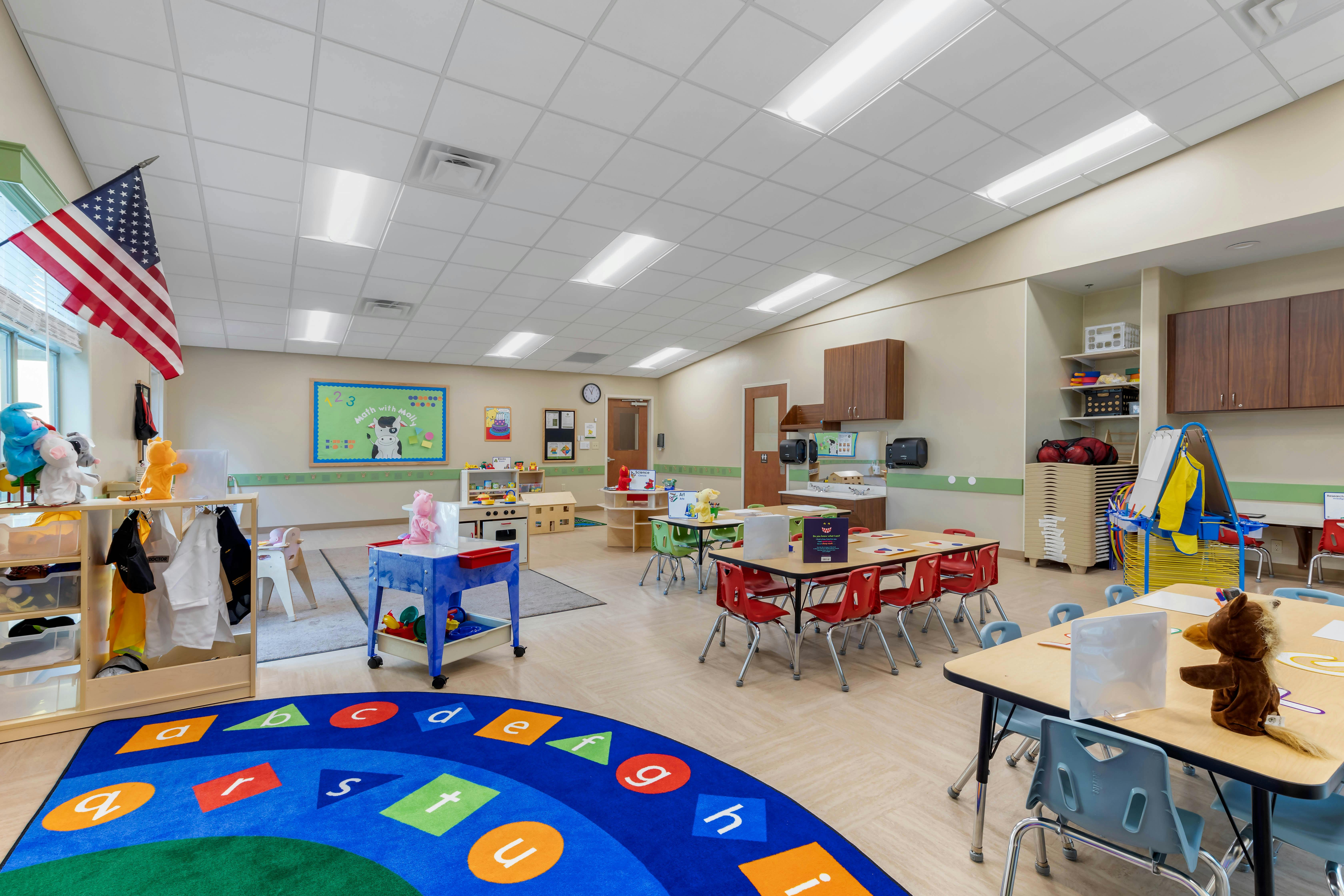 Classroom with tables, chairs, a blue alphabet rug, and learning materials