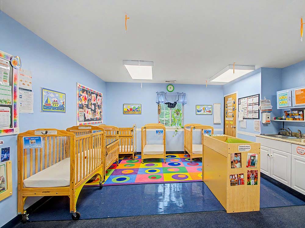Cribs in a daycare room with a colorful playmat