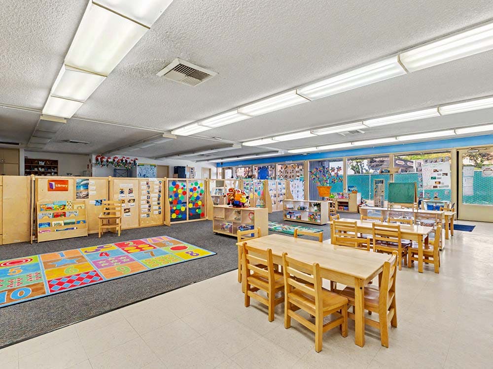 Empty classroom with small wooden tables and chairs, and a colorful rug
