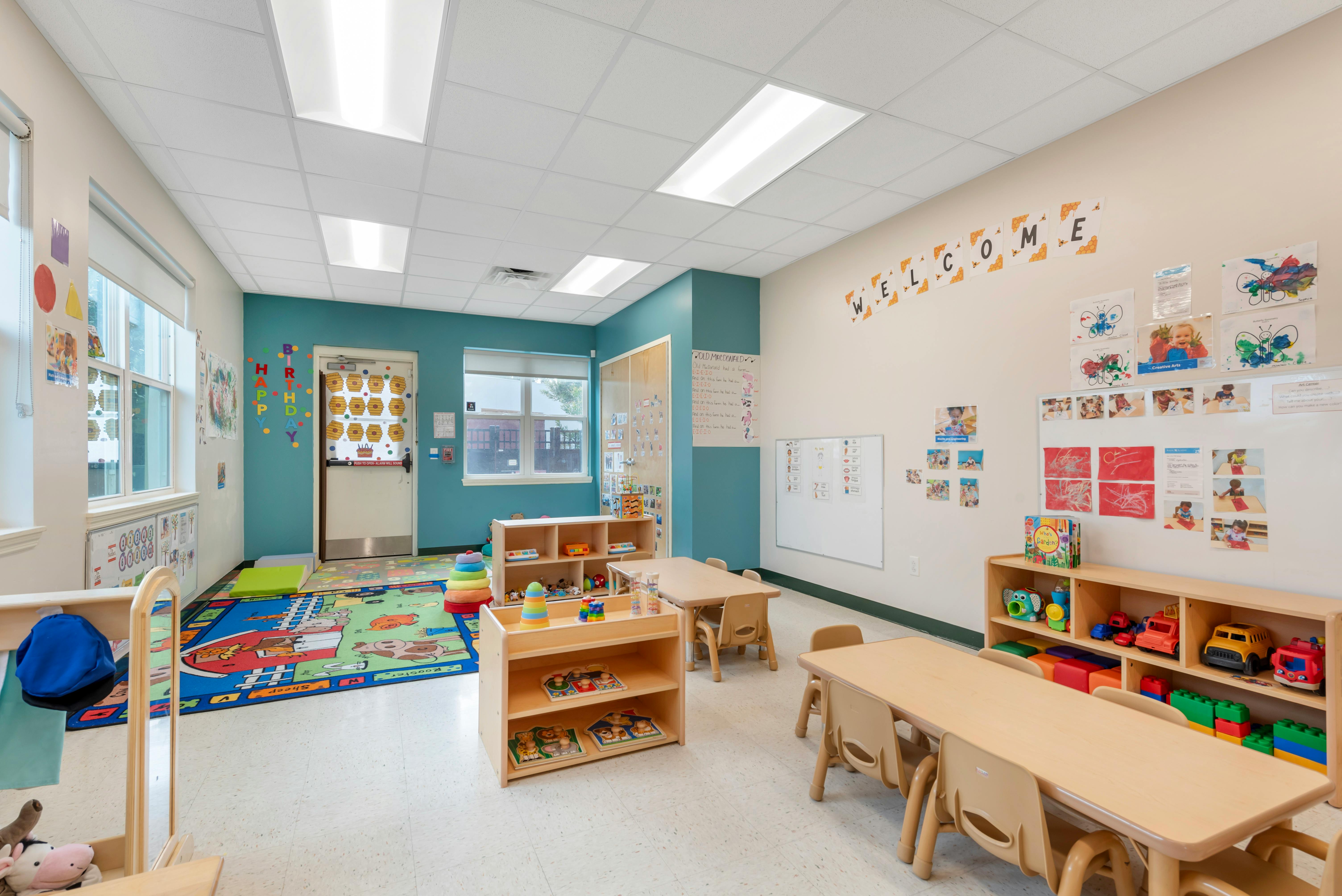 Empty classroom with small tables, chairs, and shelves with toys