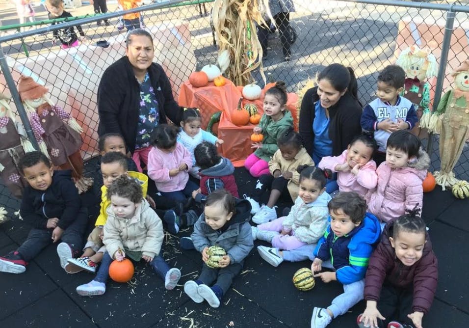 Two people with a group of children sitting on the ground with pumpkins