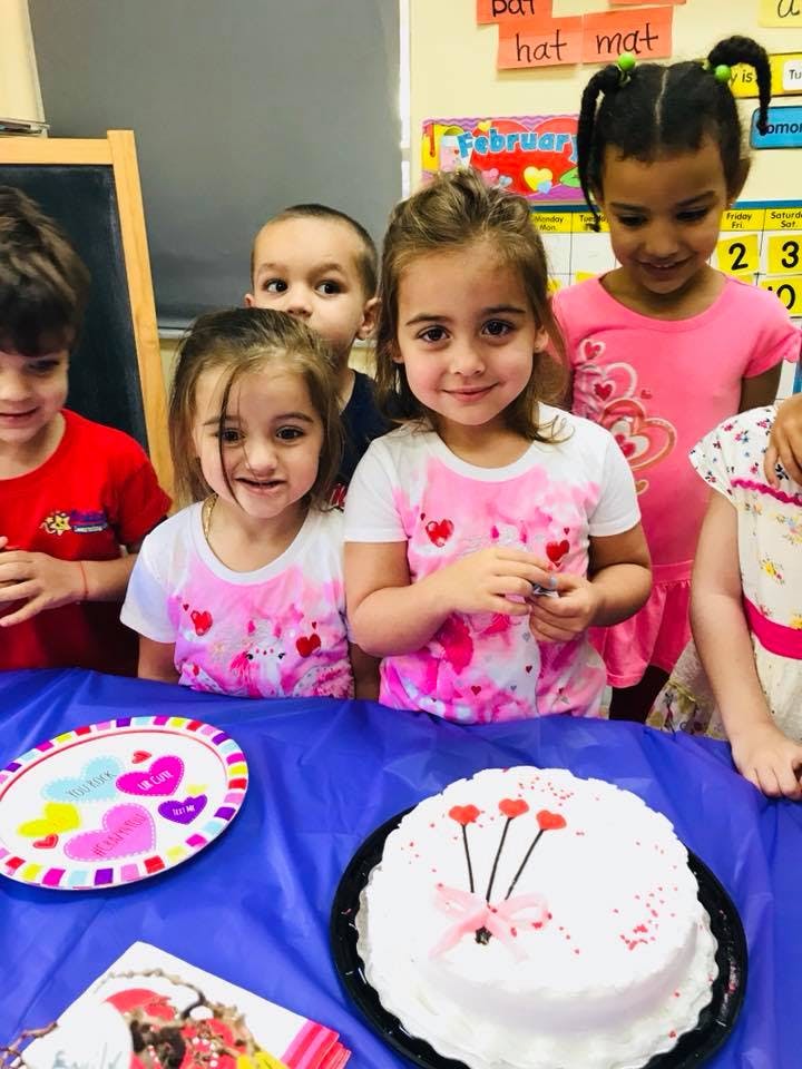 Children gathered around a table with a cake and paper plate