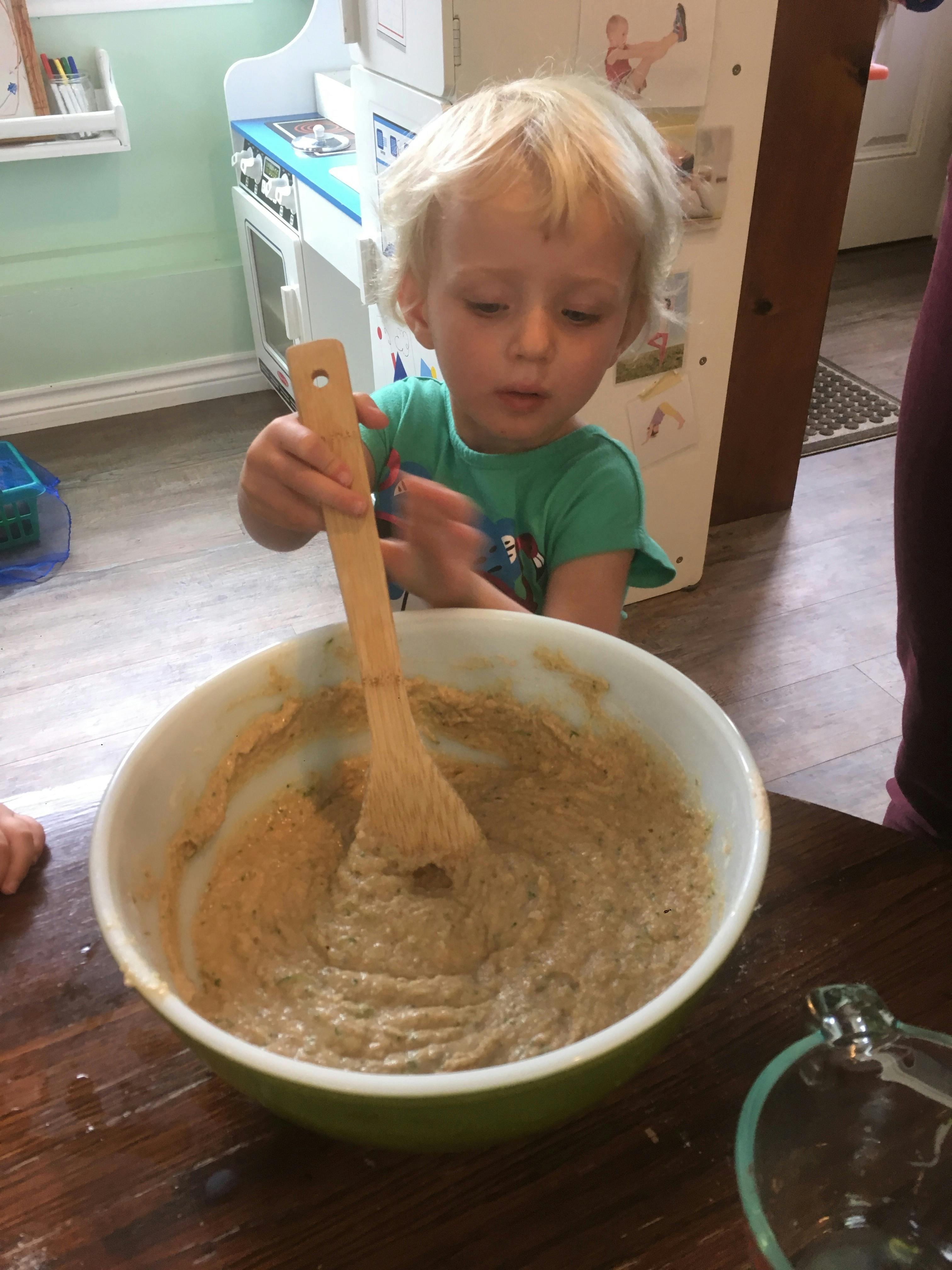 Child stirring batter in a bowl with a wooden spoon