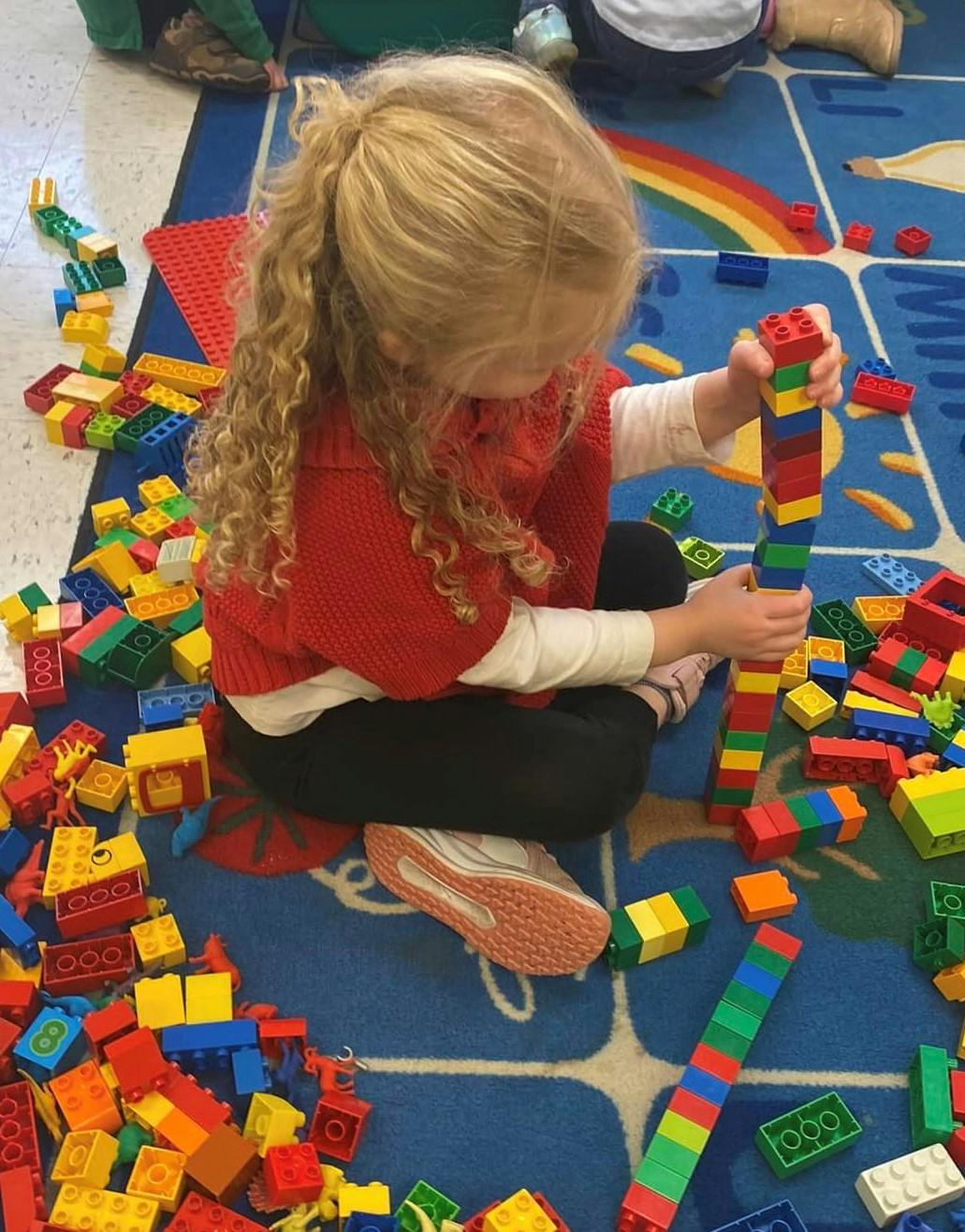 Child building a tower with colorful plastic blocks on a blue rug