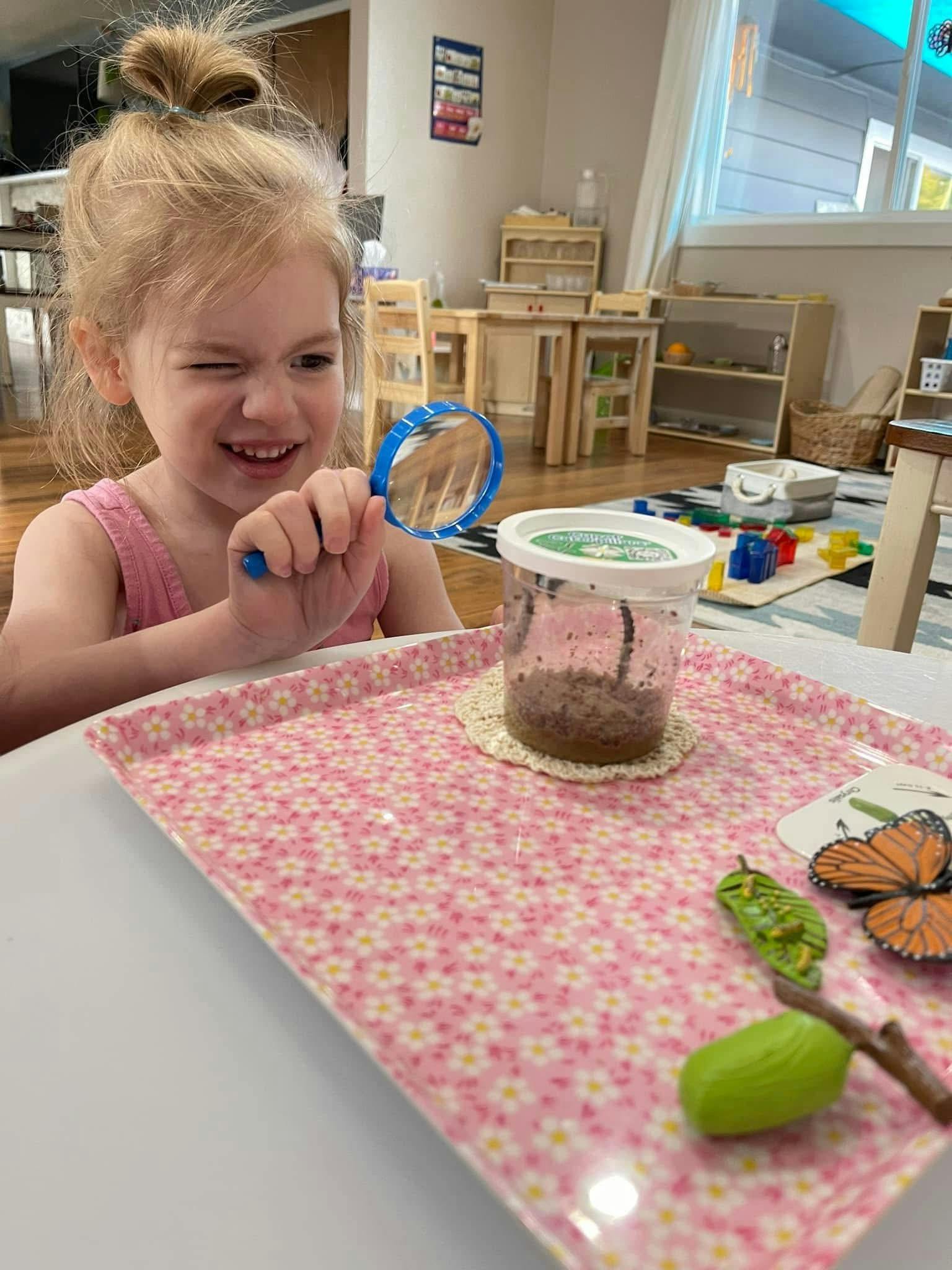 Child looking through a magnifying glass at a container on a tray