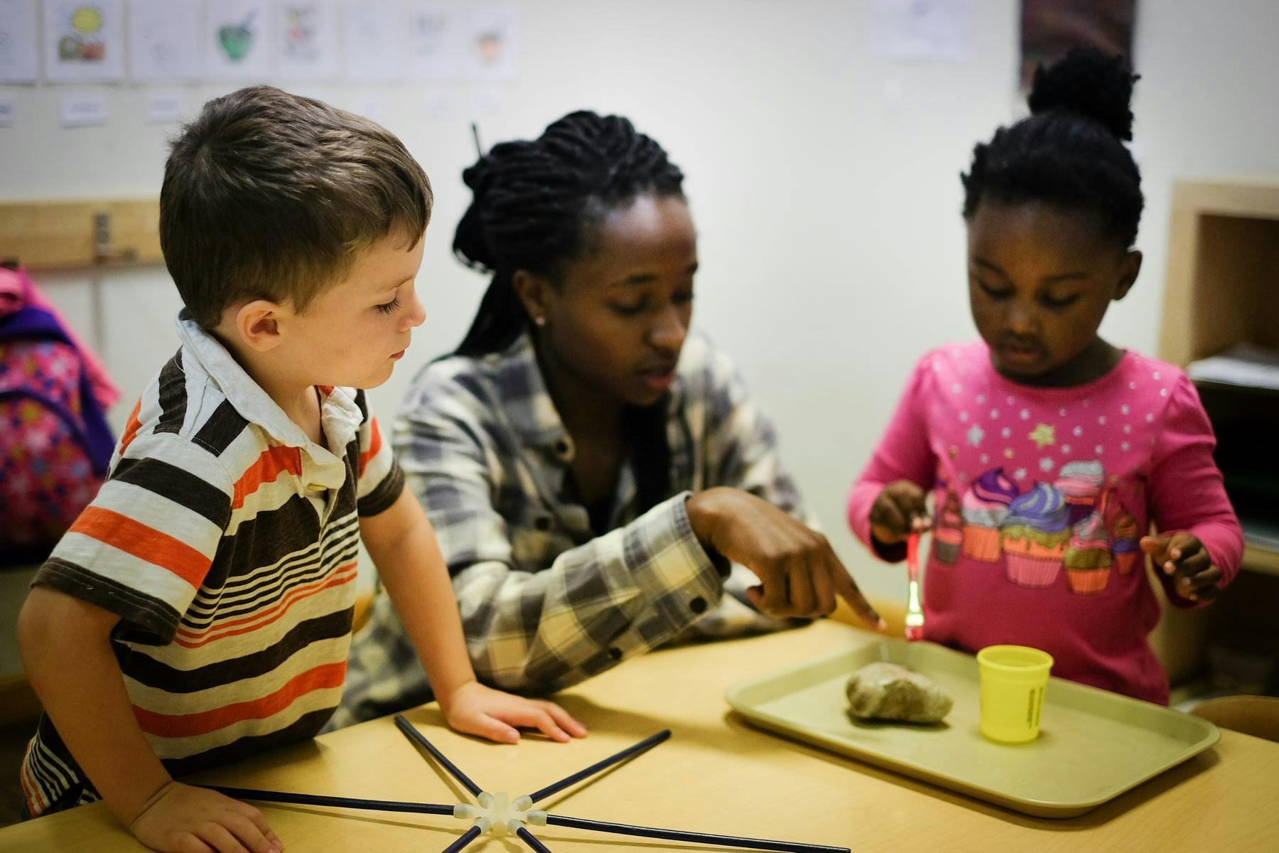 Adult and two children at a table with a tray and cup