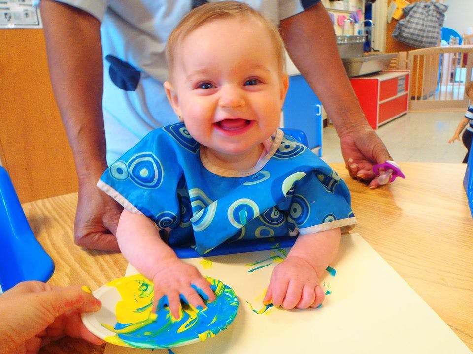 Child in a blue smock finger painting with blue and yellow paint