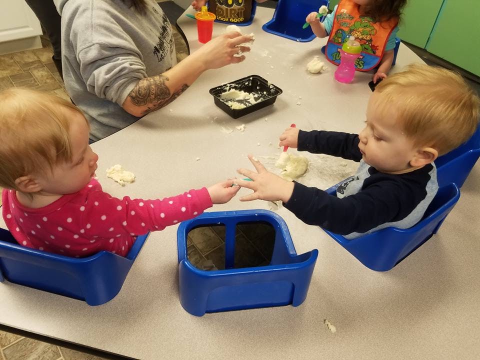 Two children in blue seats reaching for each other across a table