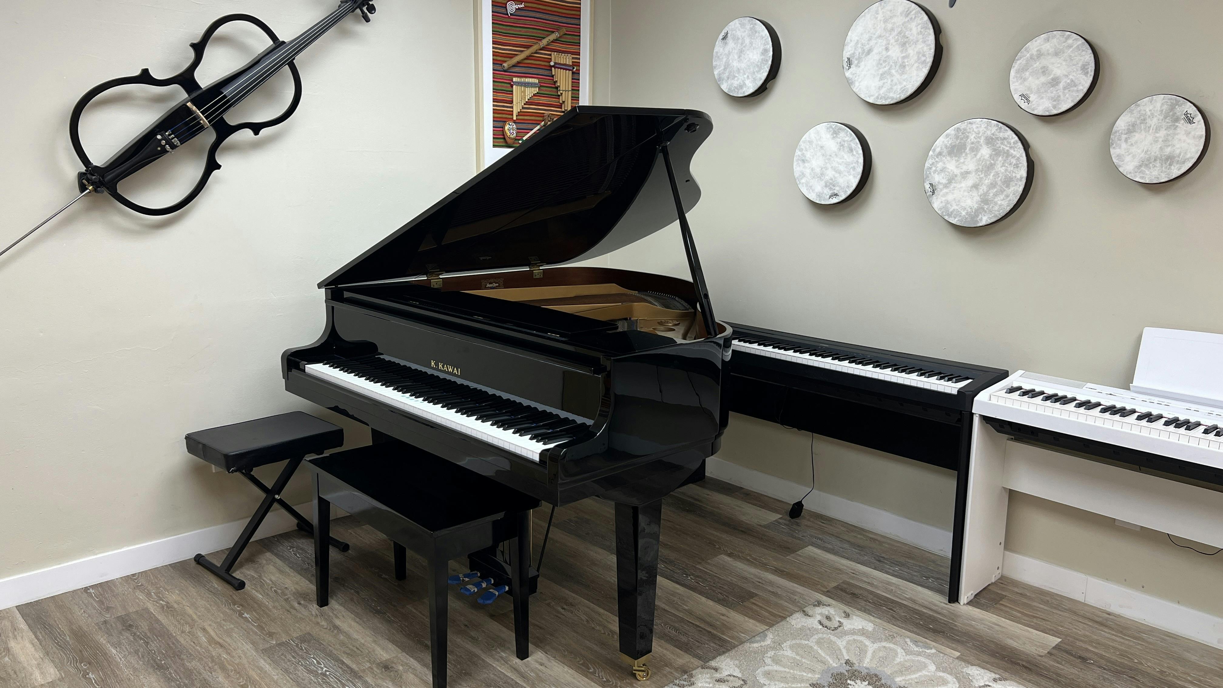 Grand piano with bench, two digital pianos, and drums mounted on a wall