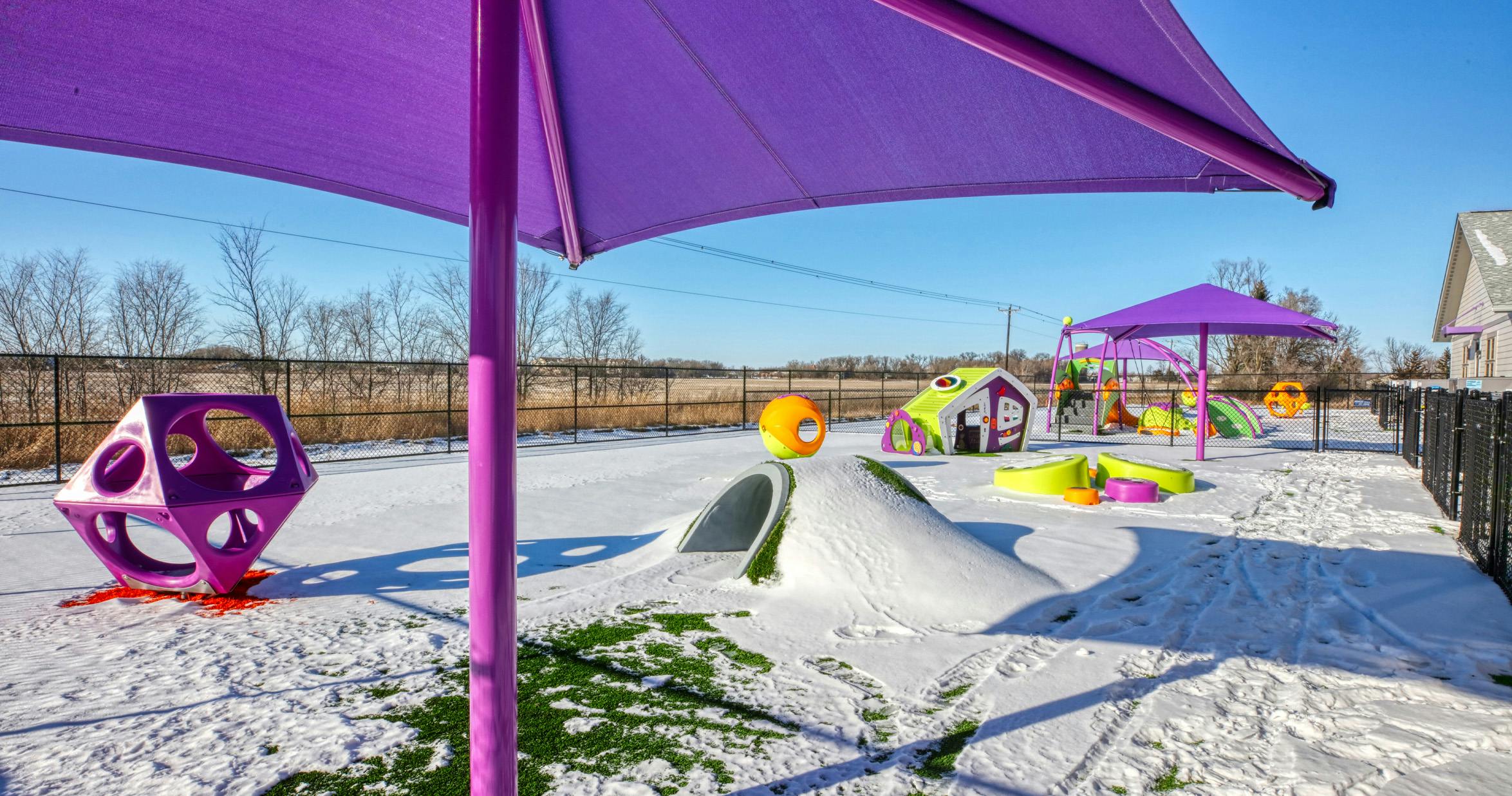 Playground covered in snow with colorful structures and purple shade covers