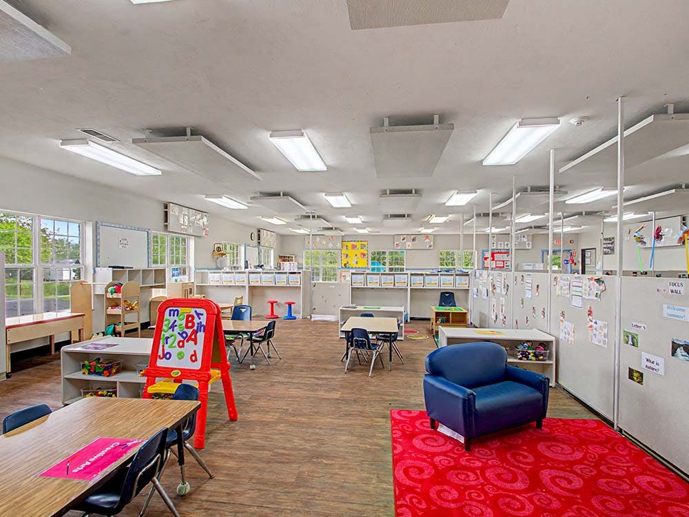 Empty colorful preschool classroom with tables, chairs, and play areas