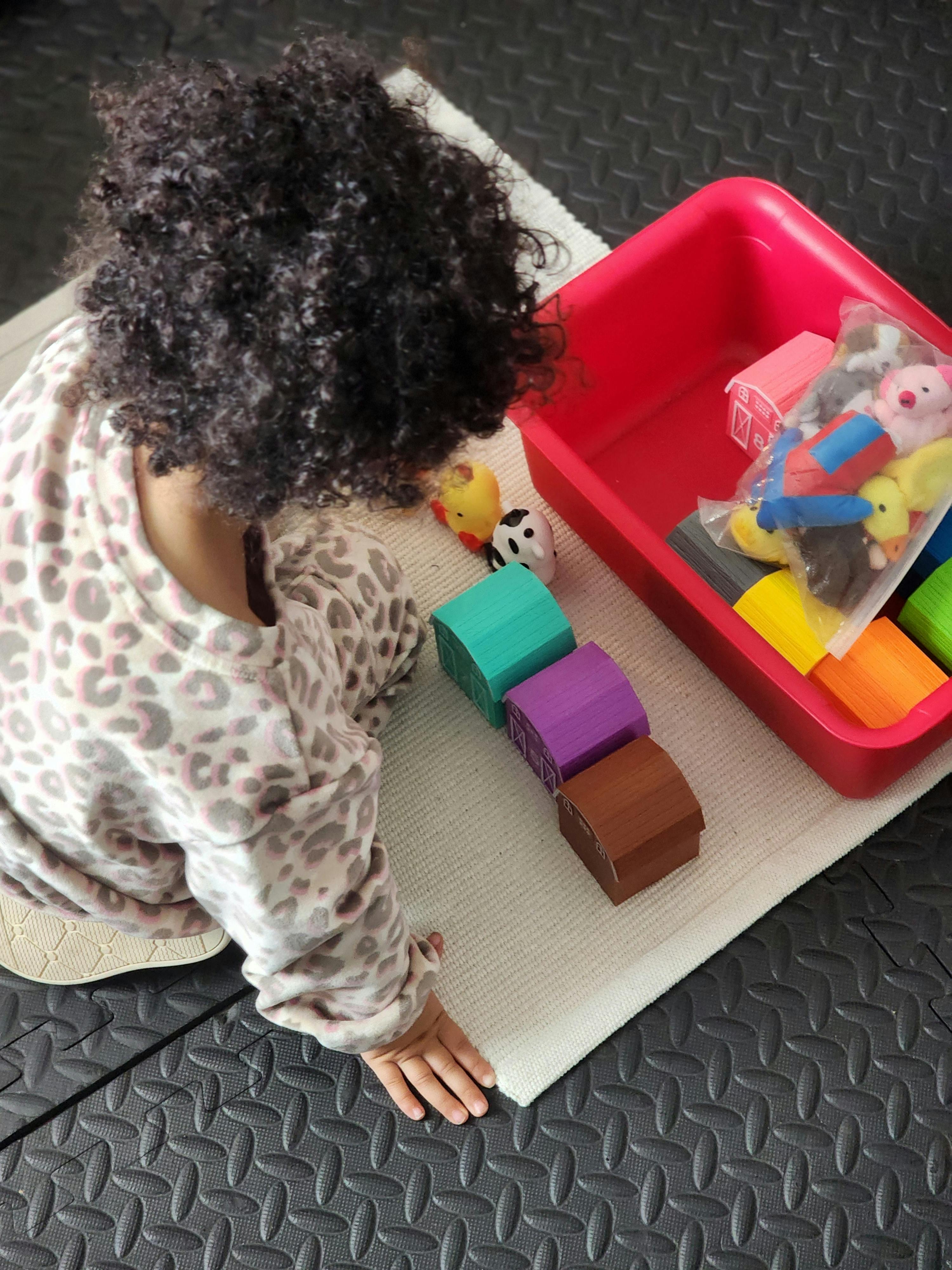 Child on the floor, hand reaching towards colored wooden blocks