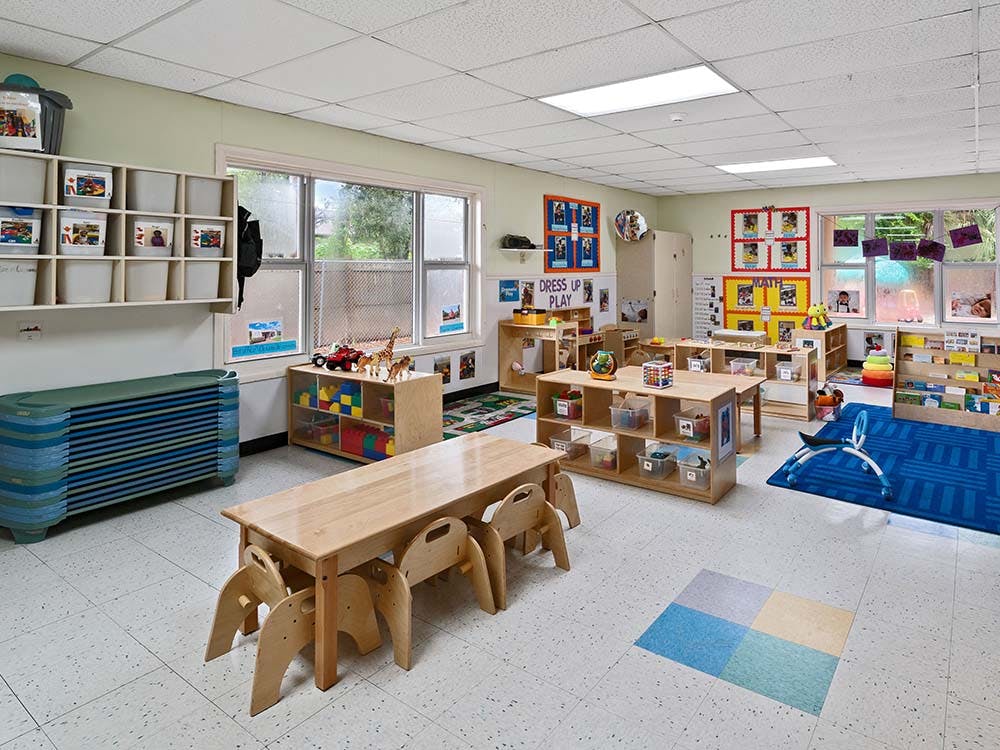 Empty colorful preschool classroom with small tables, chairs, and play areas