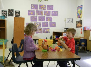Two children playing with toys at a table in a classroom