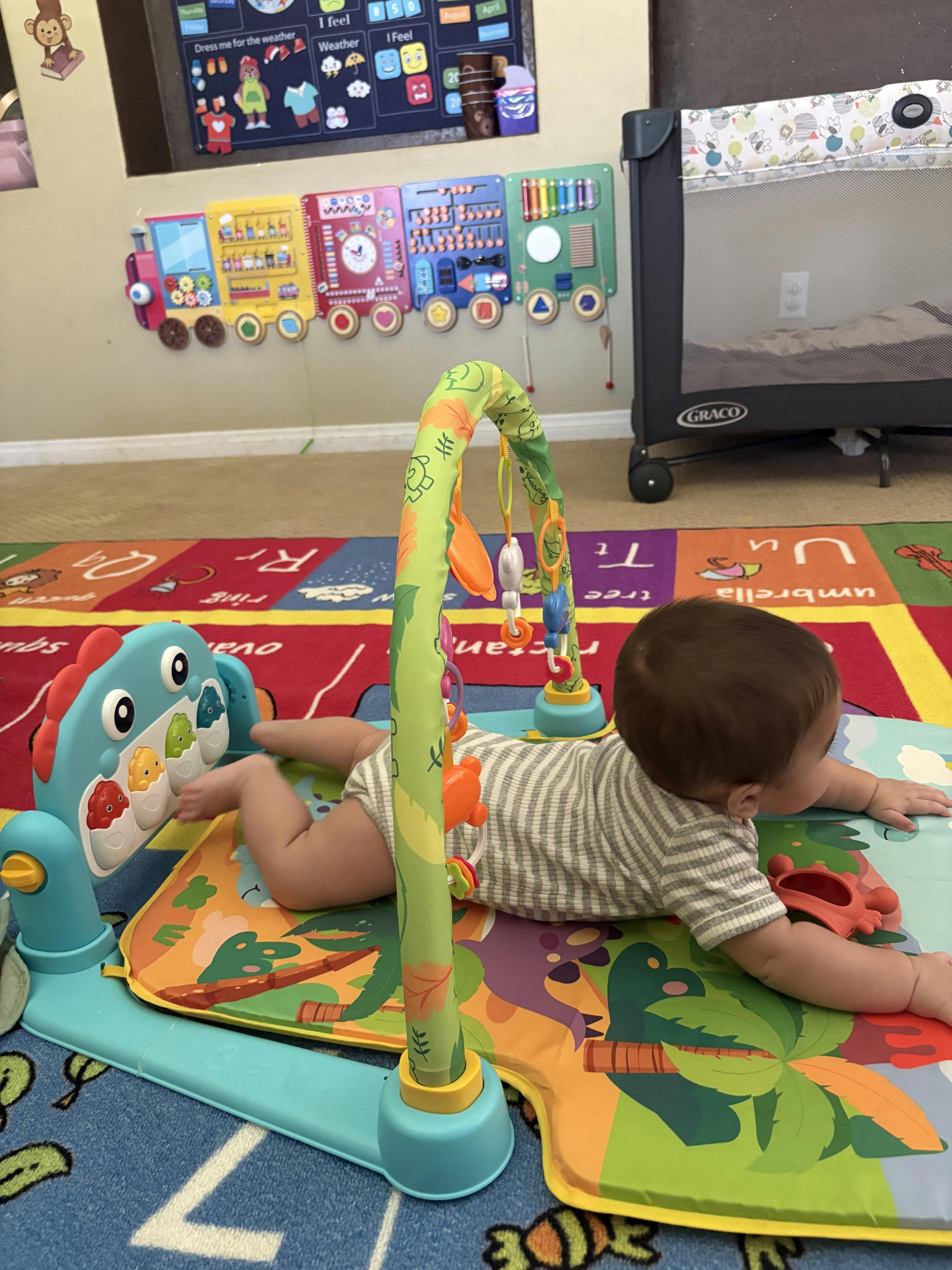 Child lying on stomach on a play mat with hanging toys in a room