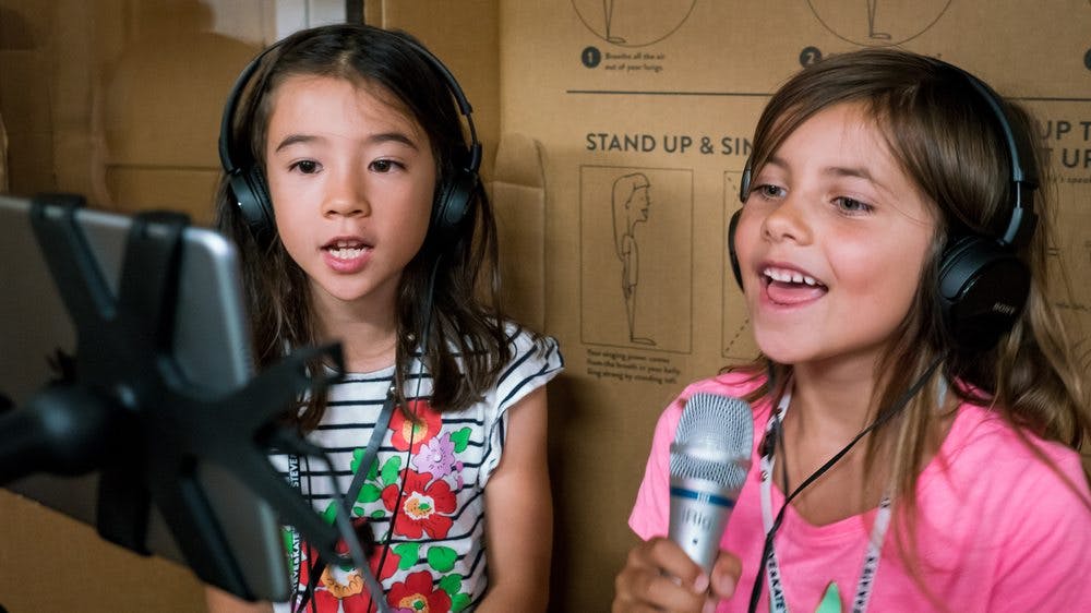 Two children wearing headphones, one singing into a microphone