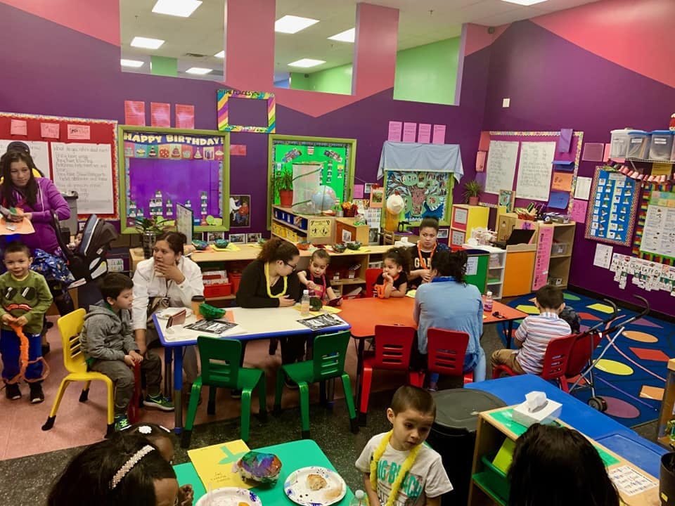 Adults and children sitting at tables in a colorful classroom