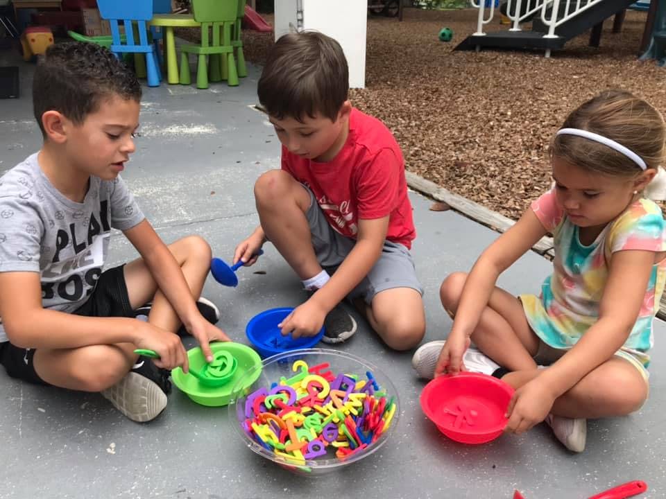 Three children playing with colorful plastic letters and bowls