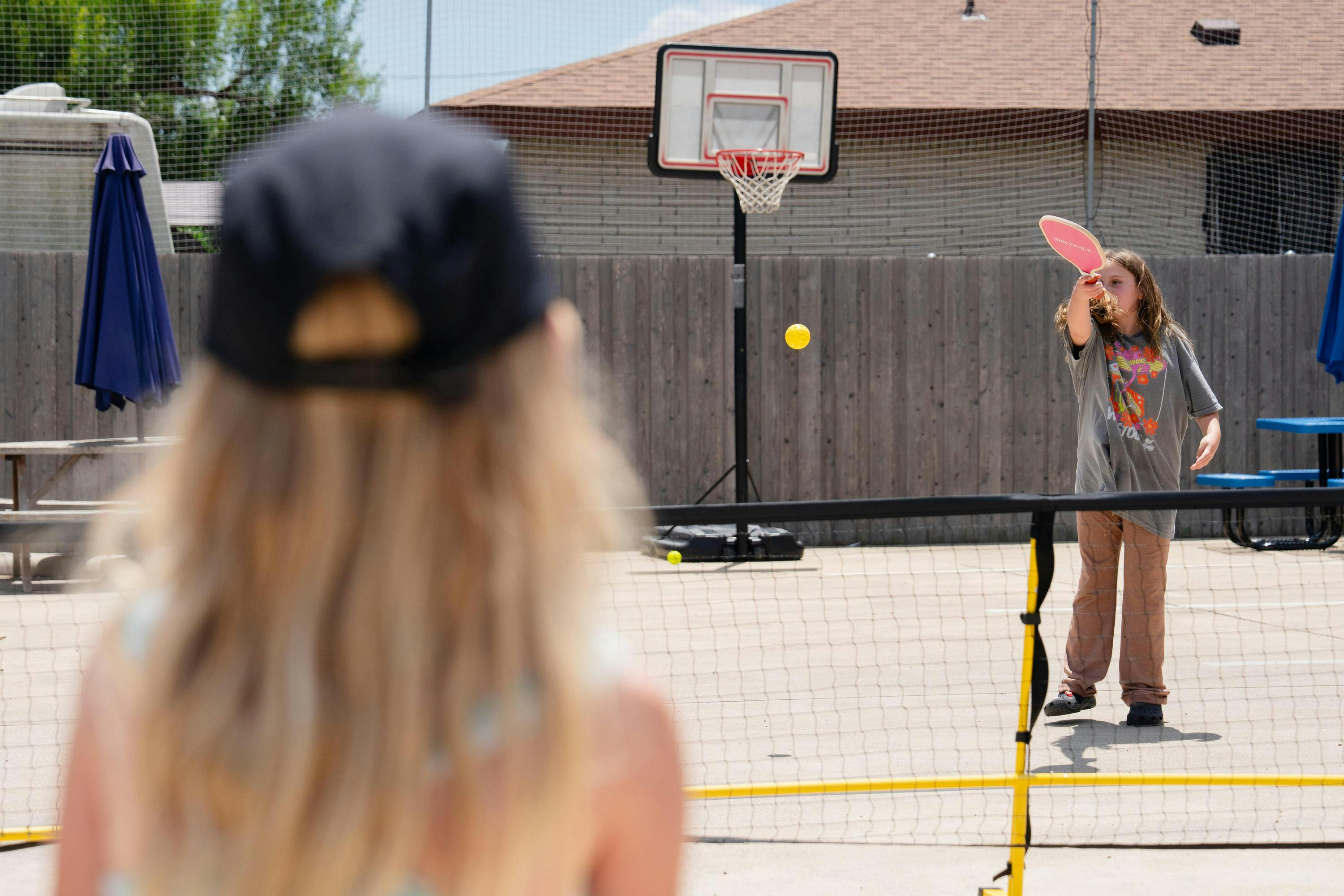 Child playing pickleball with a pink paddle, a yellow ball in mid-air