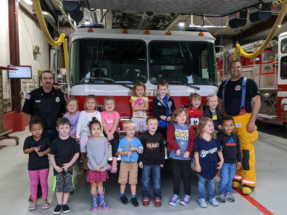 Two people and a group of children in front of a fire truck
