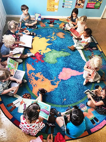 Children sitting on a world map rug reading books