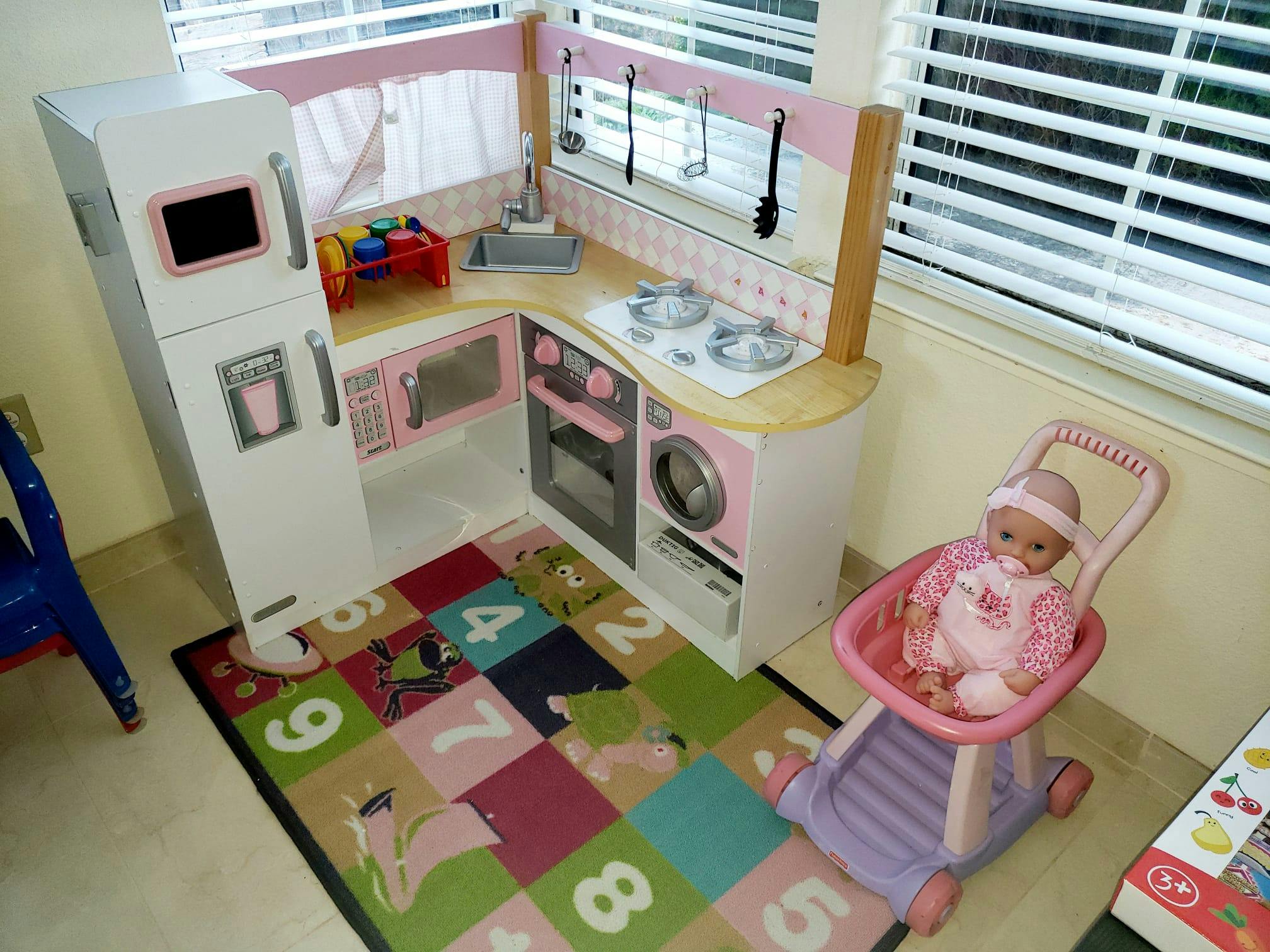 Doll in a stroller next to a play kitchen set