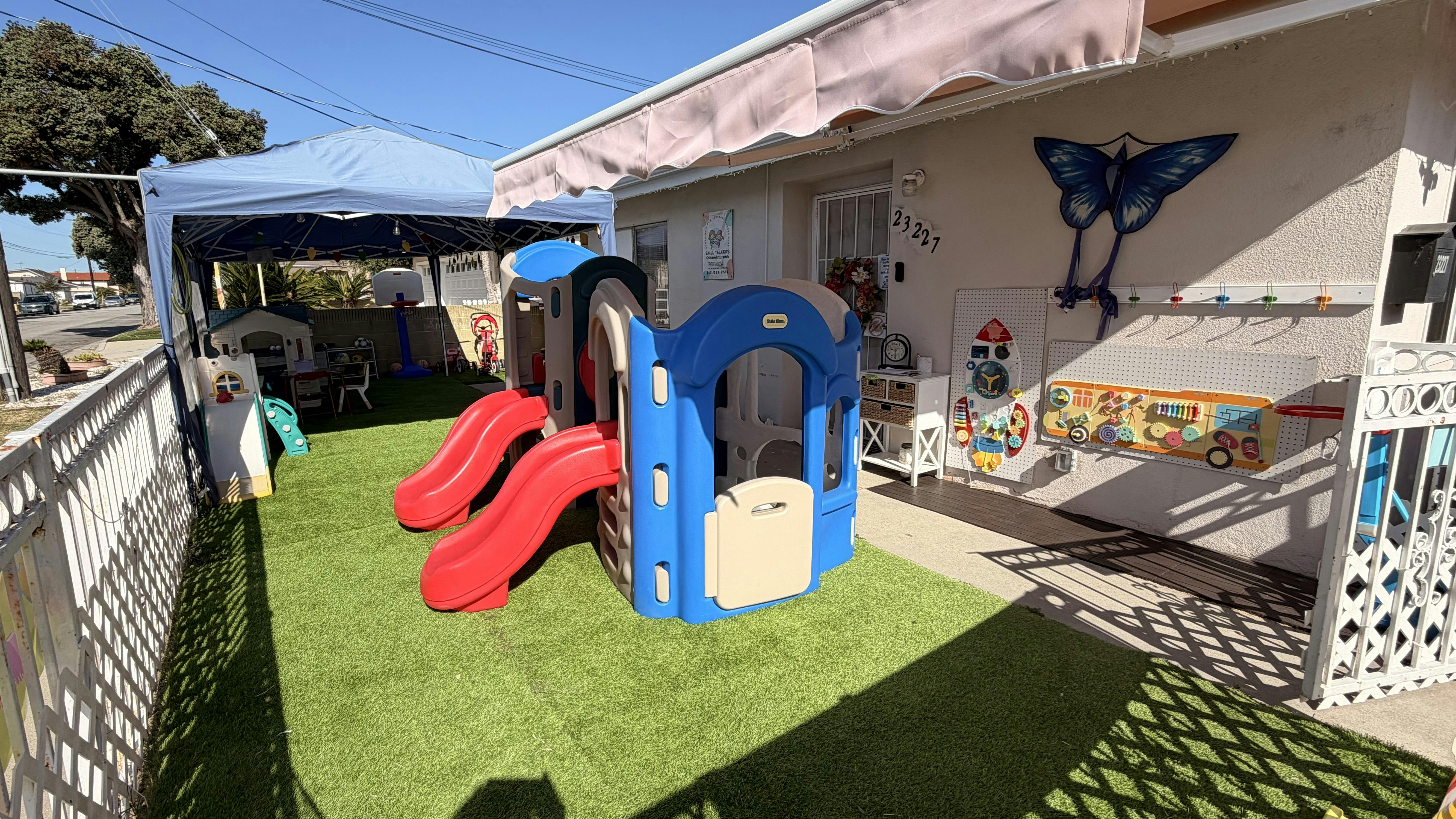 Outdoor play area with artificial turf, a plastic play structure, and covered seating