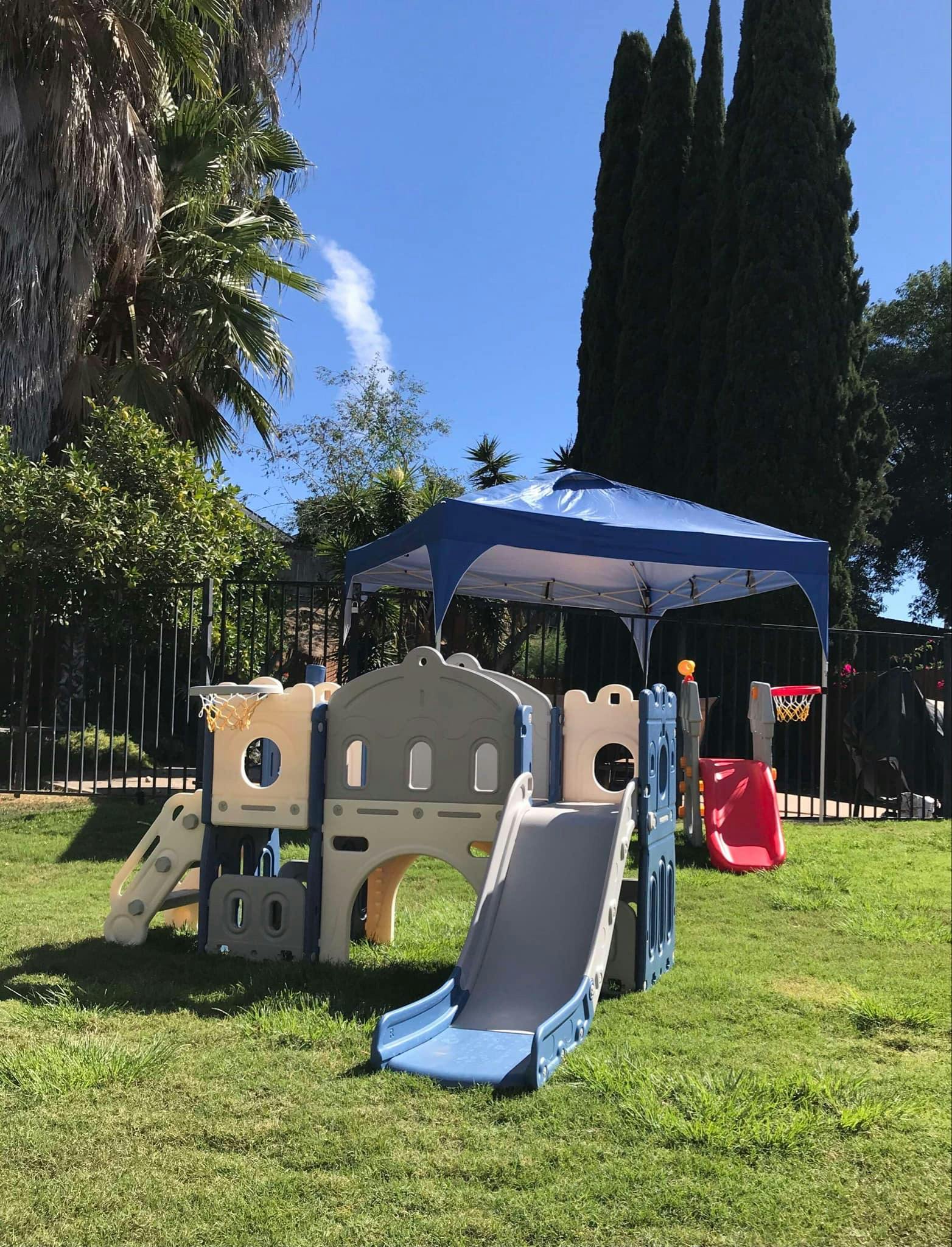 Play structure with slides and a blue canopy in a grassy area