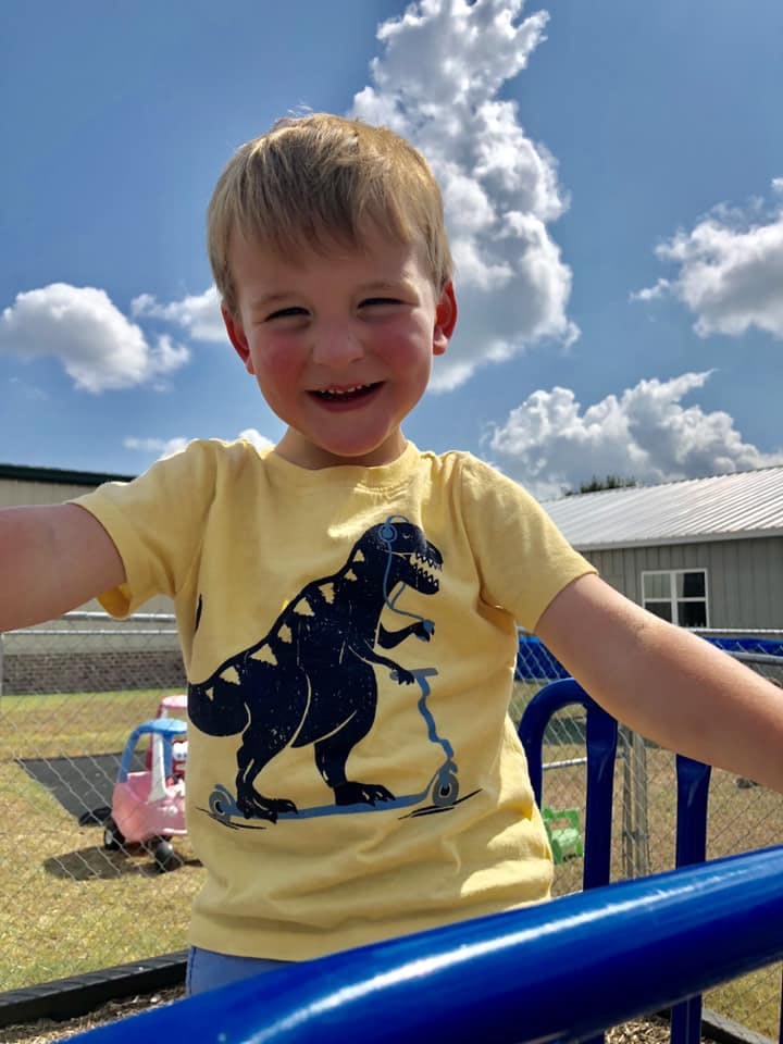 Child in a yellow shirt with a dinosaur on a scooter, outdoors