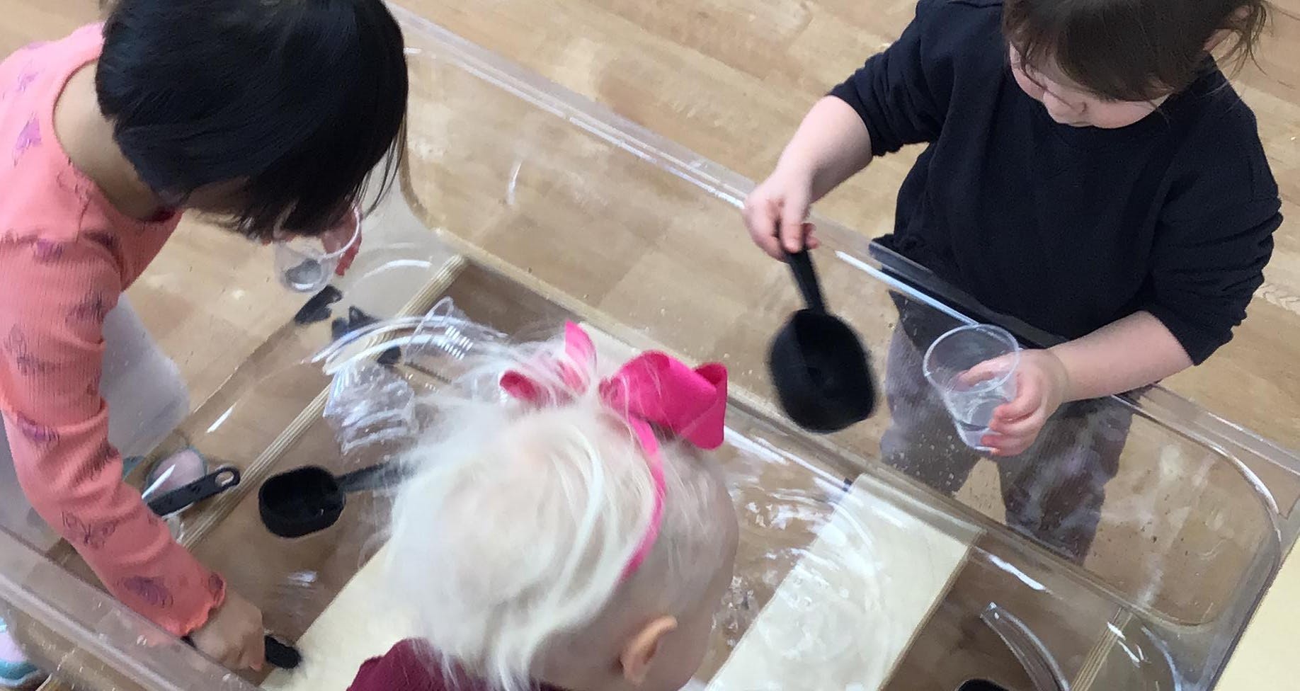 Children playing with water and scoops in a clear bin