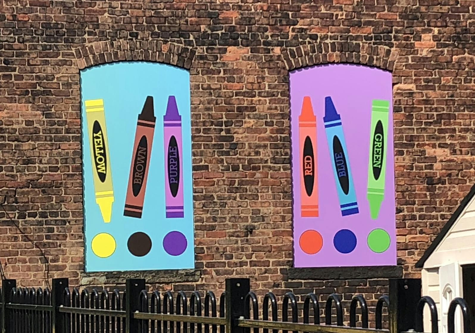 Crayon drawings with color names in window-like frames on a brick wall