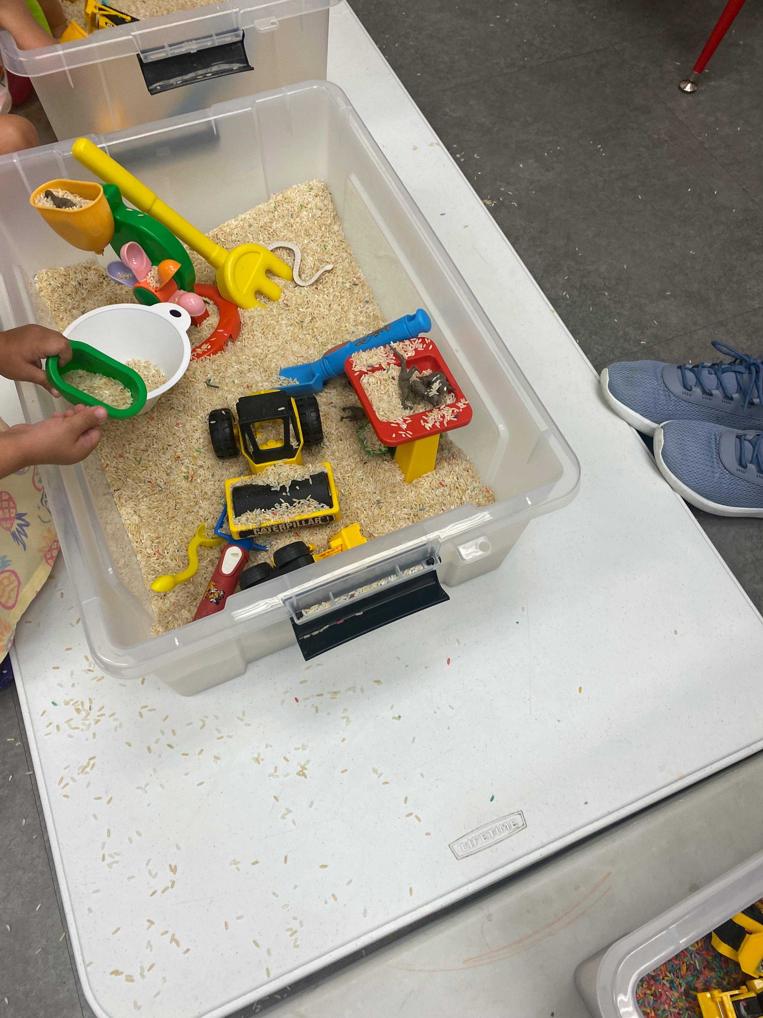 Child's hands playing with toys in a sensory bin filled with rice