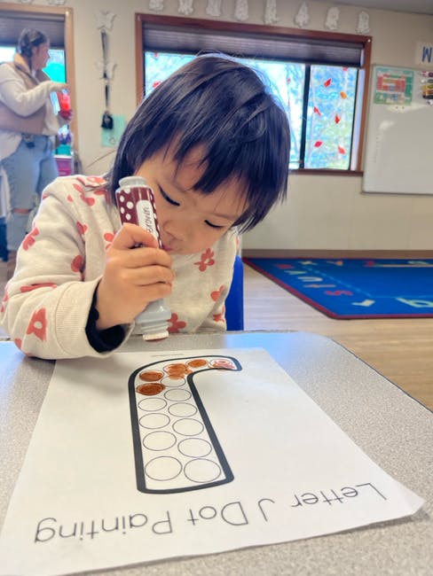 Child using a dot marker to fill in circles on a paper with the letter J