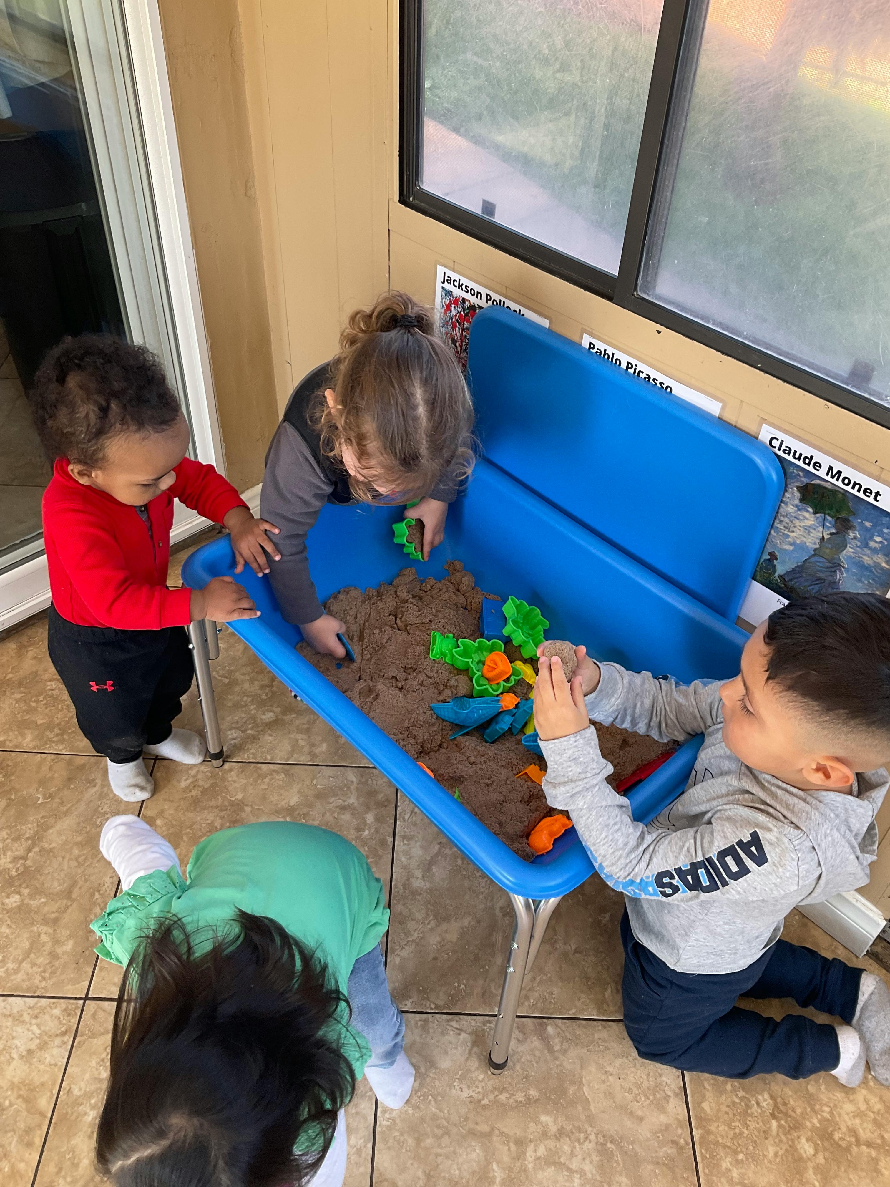 Children playing with sand and toys in a blue sand table