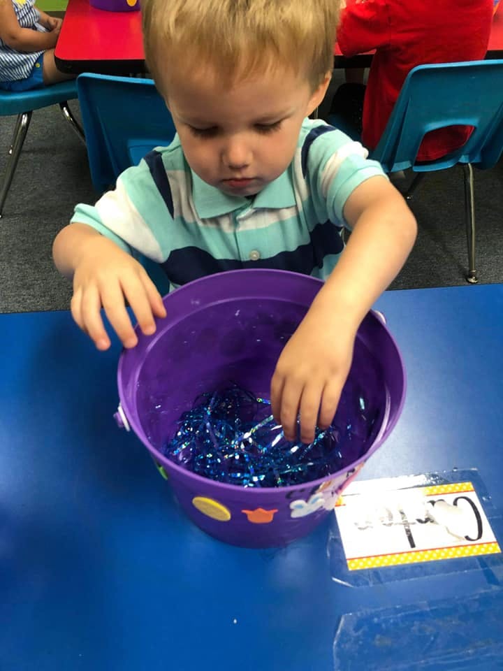 Child reaching into a purple bucket filled with blue tinsel