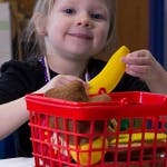 Child playing with a red shopping basket and toy fruit