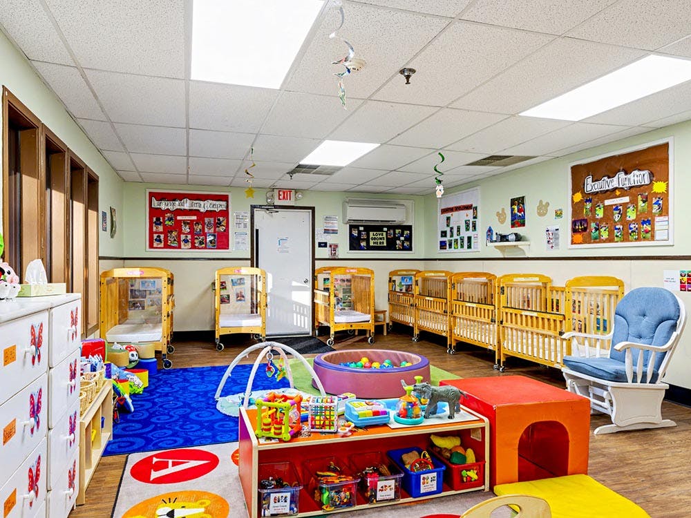 Childcare room with multiple cribs, a play area, and an "Exit" sign