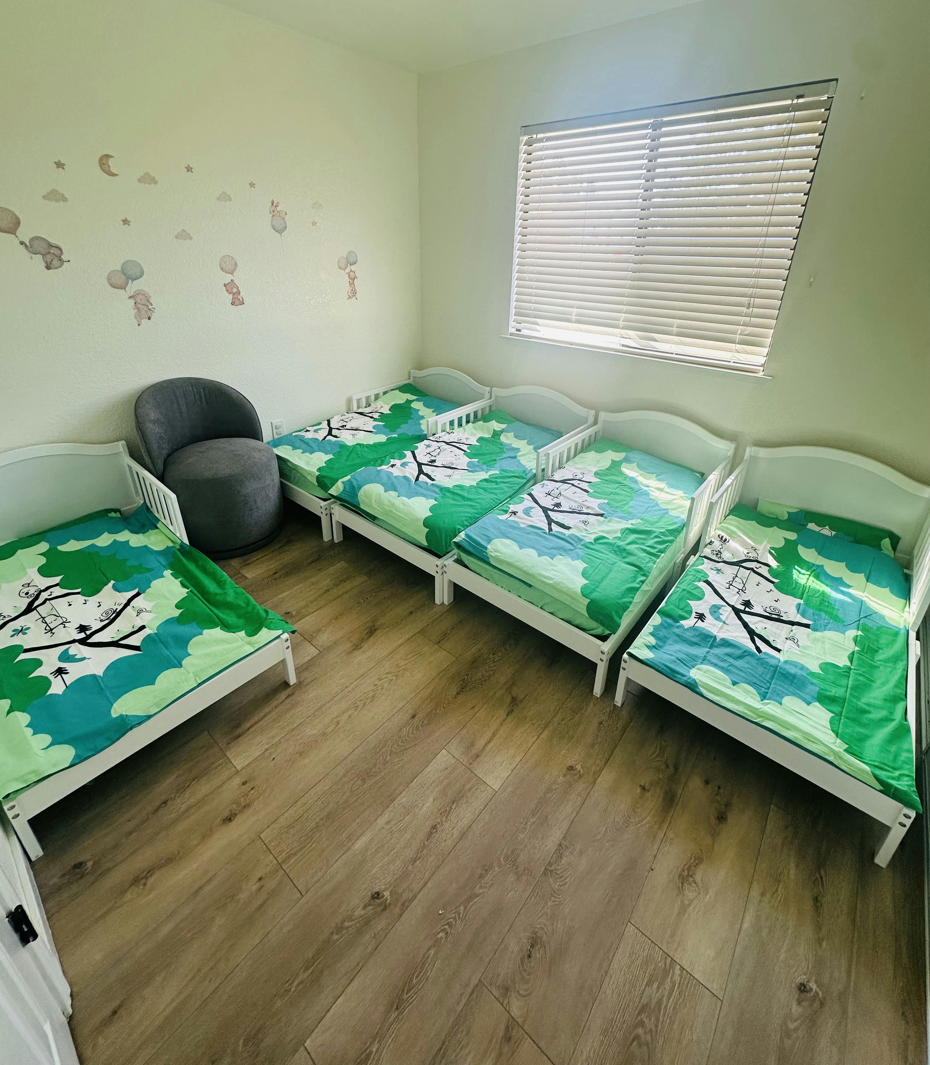 Four small white toddler beds with patterned bedding in a bedroom