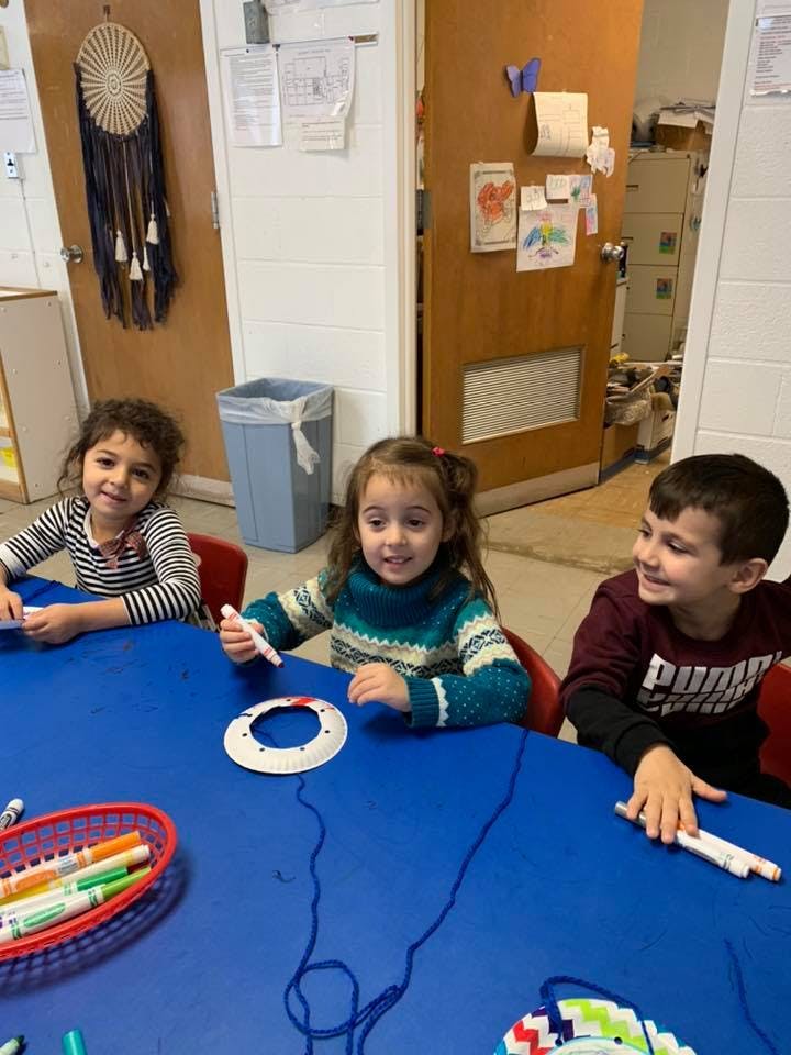 Three children sitting at a blue table with craft supplies